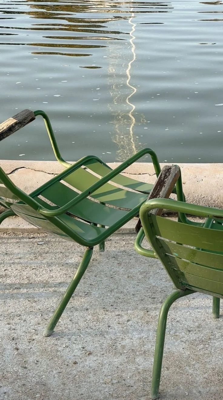 Twee groene ligstoelen aan de waterkant met een spiegeling van een mast op het water. Parijs