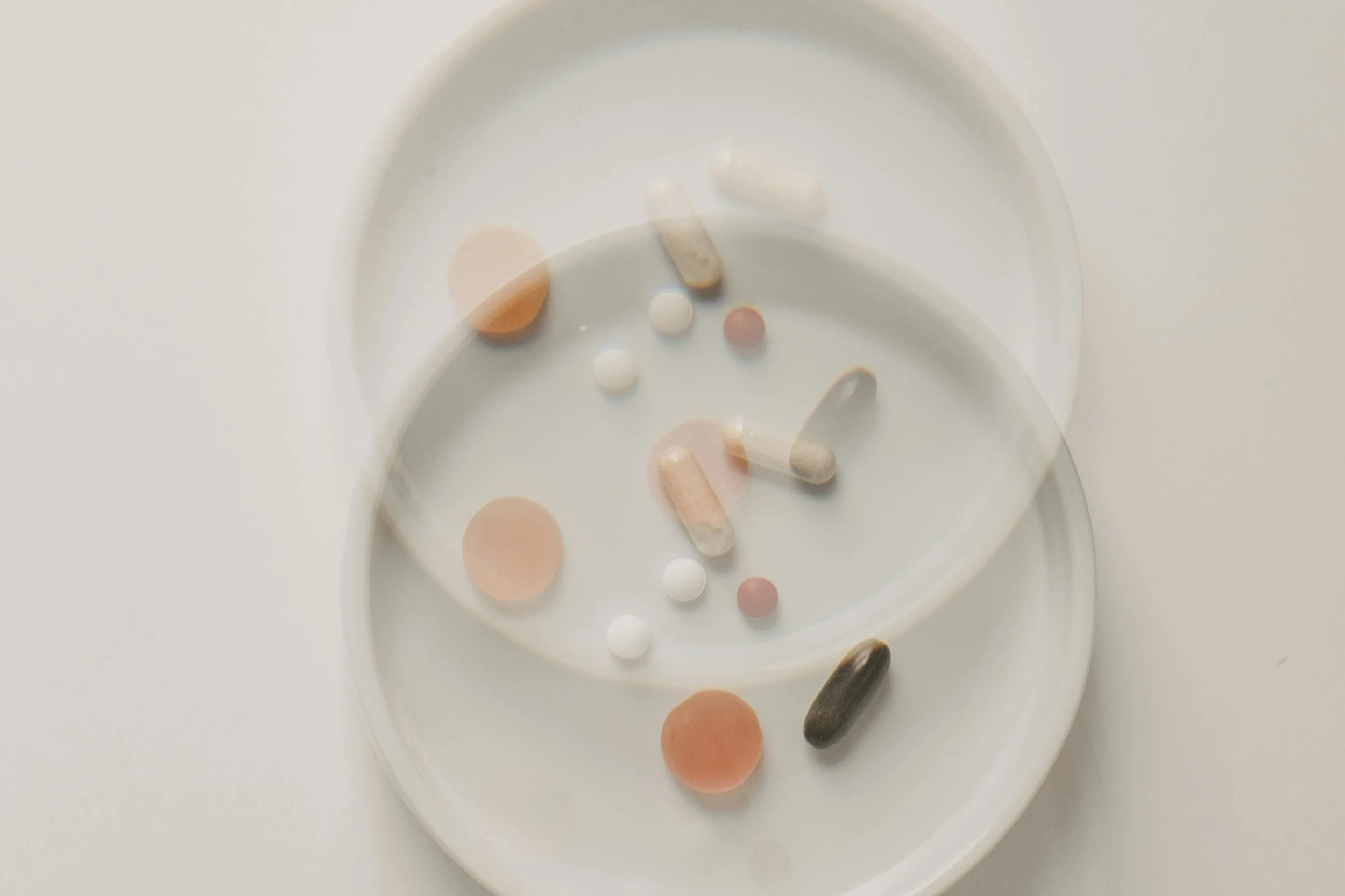 Two white medicine pill organizer trays with various pills and capsules inside, on a white surface.