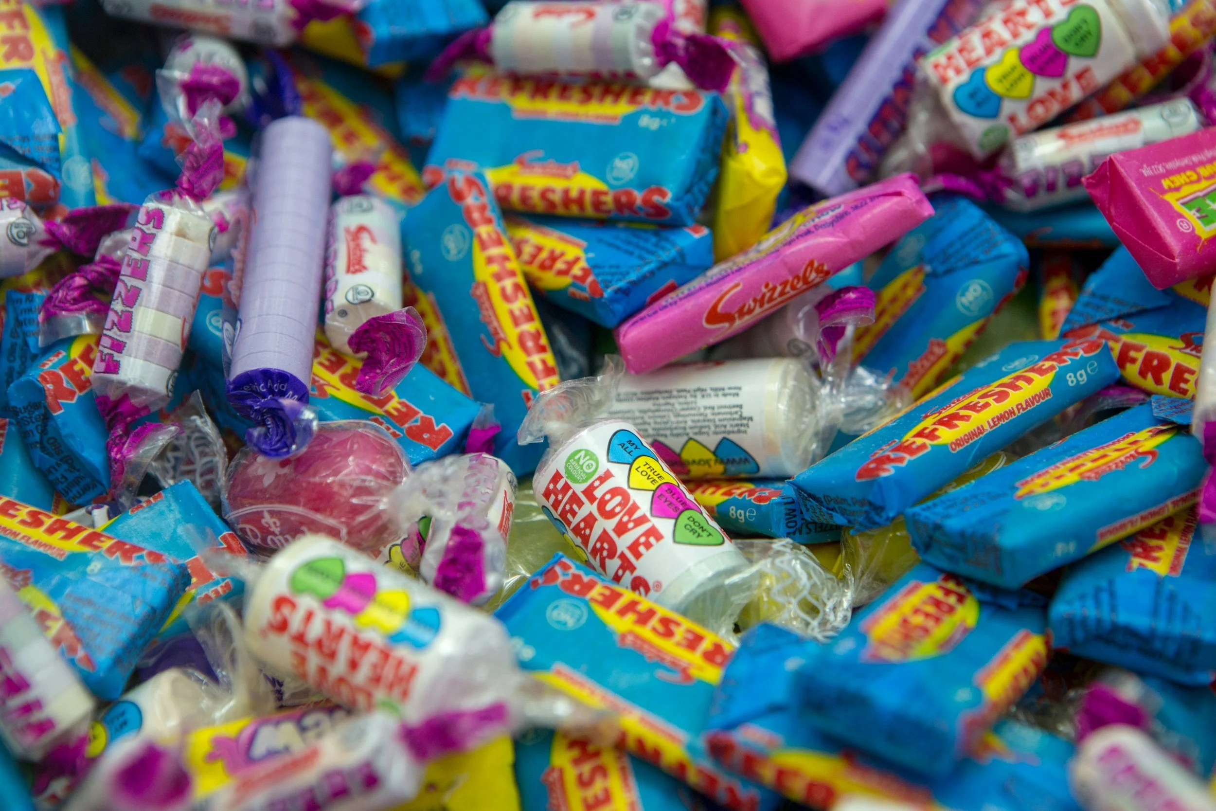 A pile of various Tutti Frutti flavored candies, including flavored sticks, small rolls, and wrapped candies with bright packaging in blue, pink, and yellow colors.