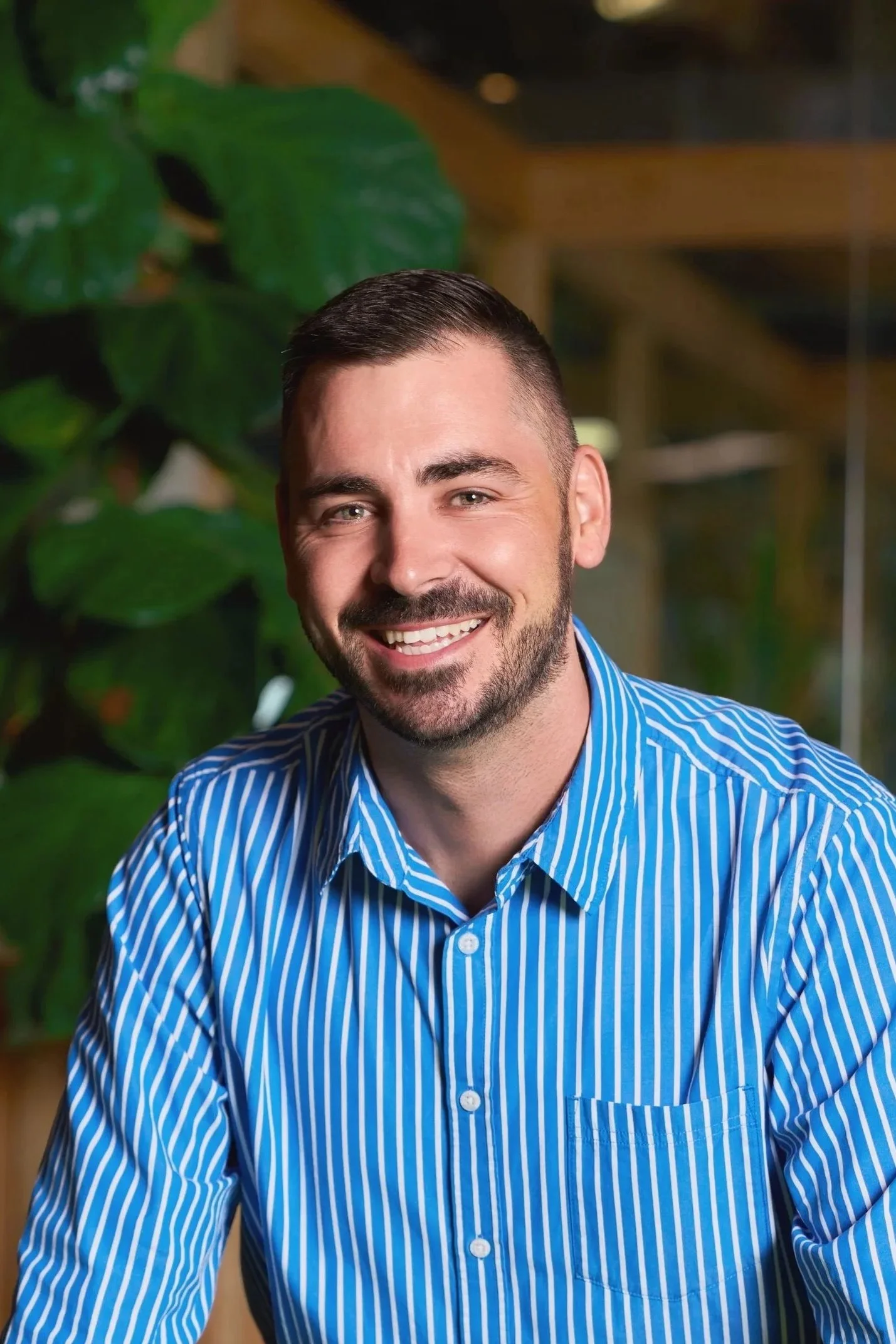Young woman with shoulder-length dark hair, smiling, wearing a black top, sitting with her chin resting on her hand in a well-lit room.