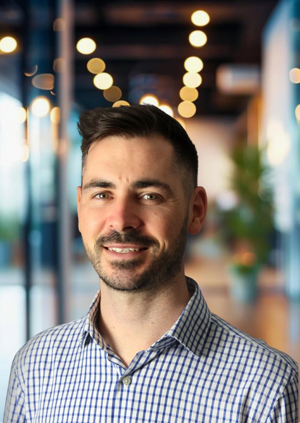 Young woman with shoulder-length dark hair, smiling, wearing a black top, sitting with her chin resting on her hand in a well-lit room.