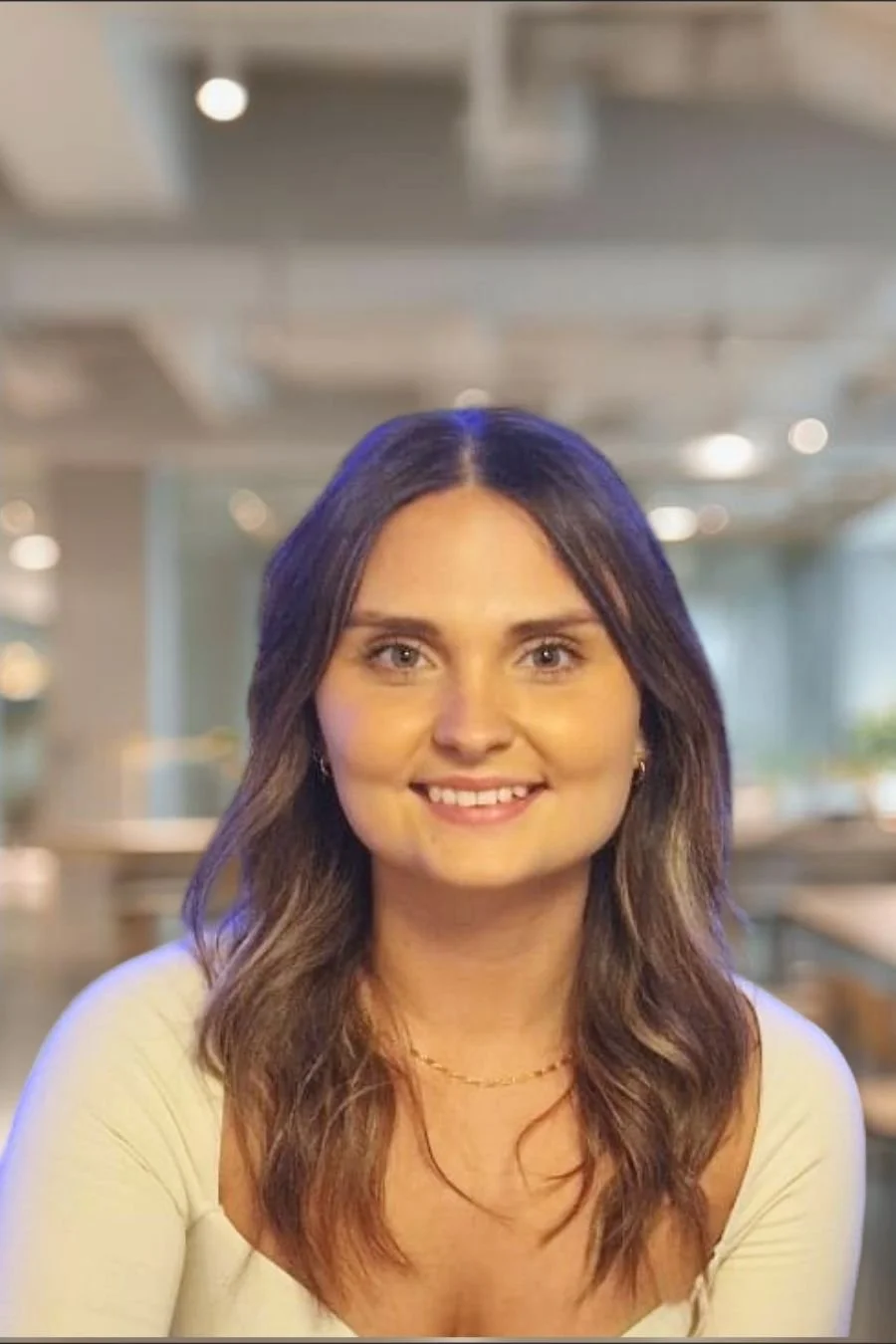 A young woman smiling and sitting at a wooden desk with her hand resting on her chin, in front of a silver HP laptop.