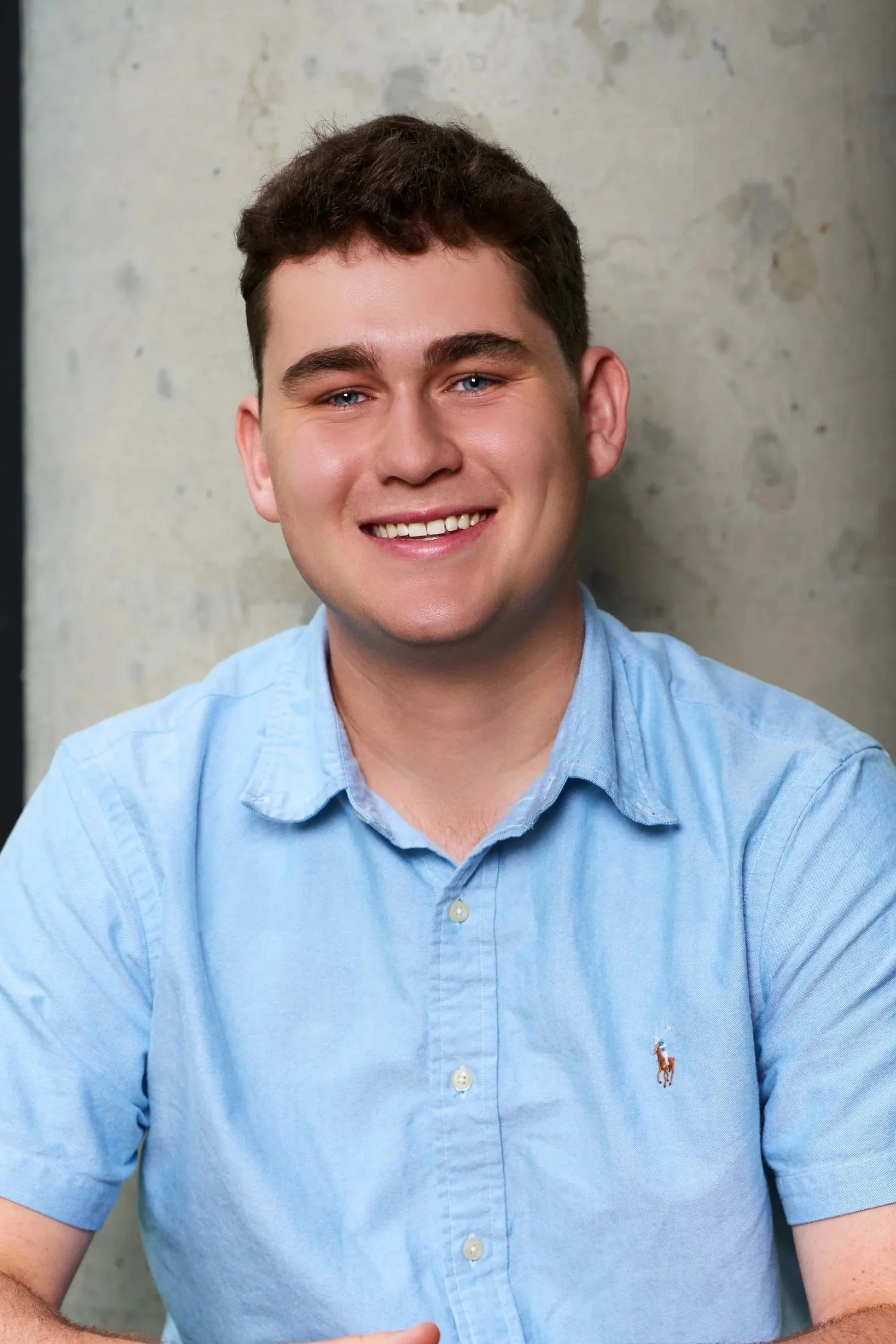 Smiling woman with shoulder-length blonde hair, wearing a black top and a necklace, indoors with warm lighting.