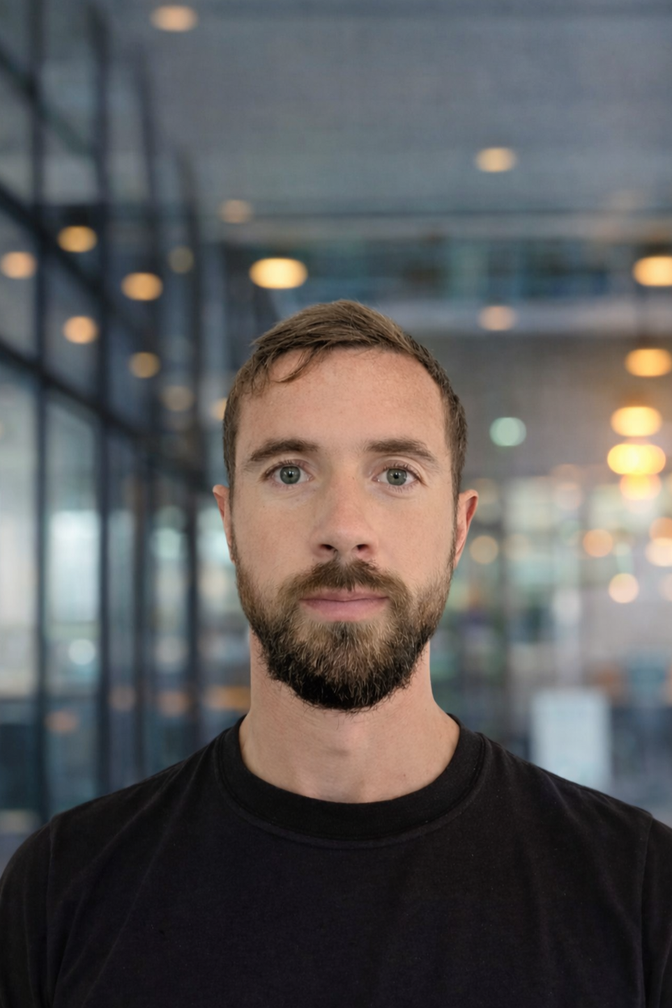 A young woman smiling and sitting at a wooden desk with her hand resting on her chin, in front of a silver HP laptop.