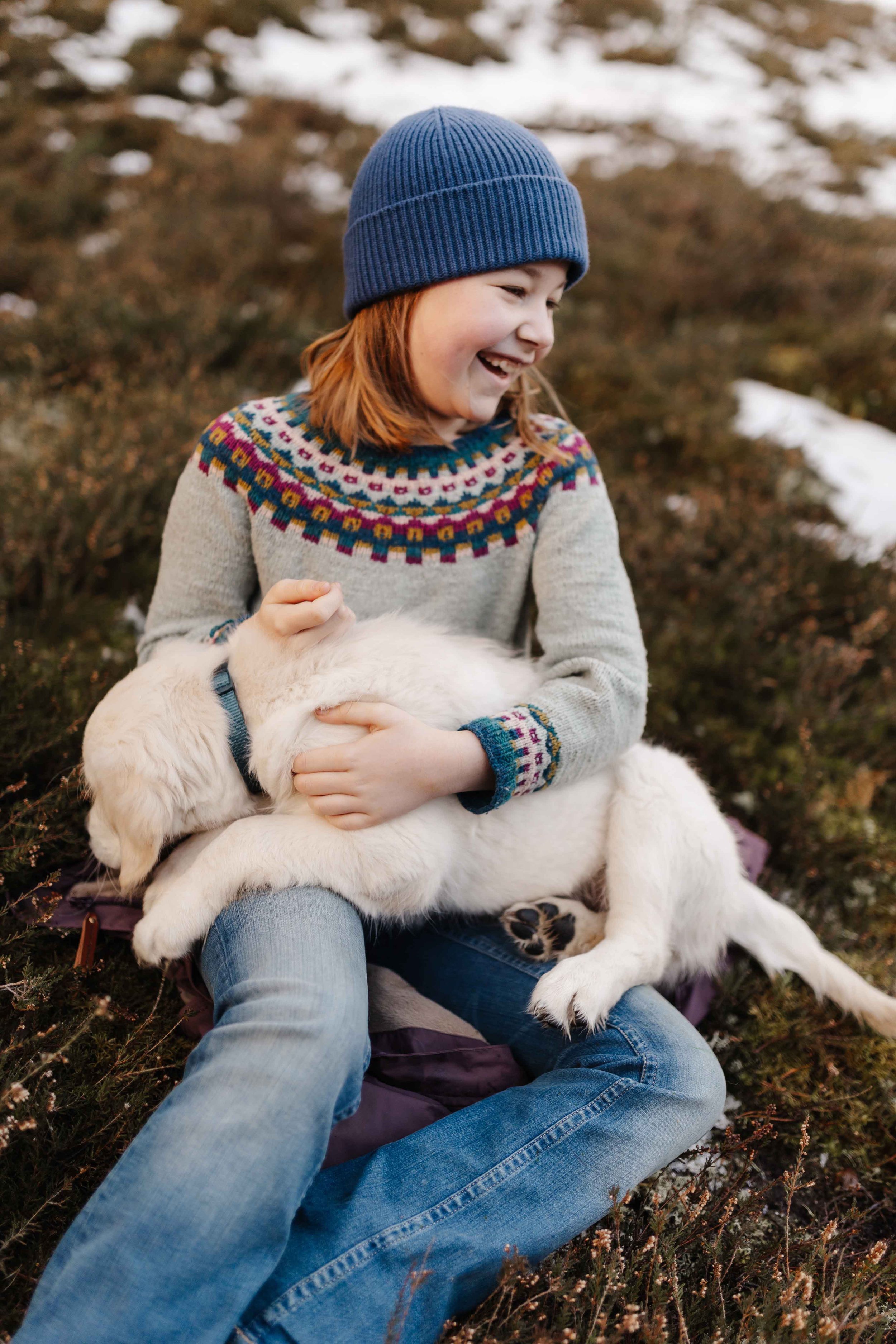 Lachendes Kind spielt im Winter mit einem Golden Retriever Welpen auf einer Wiese mit Schnee.