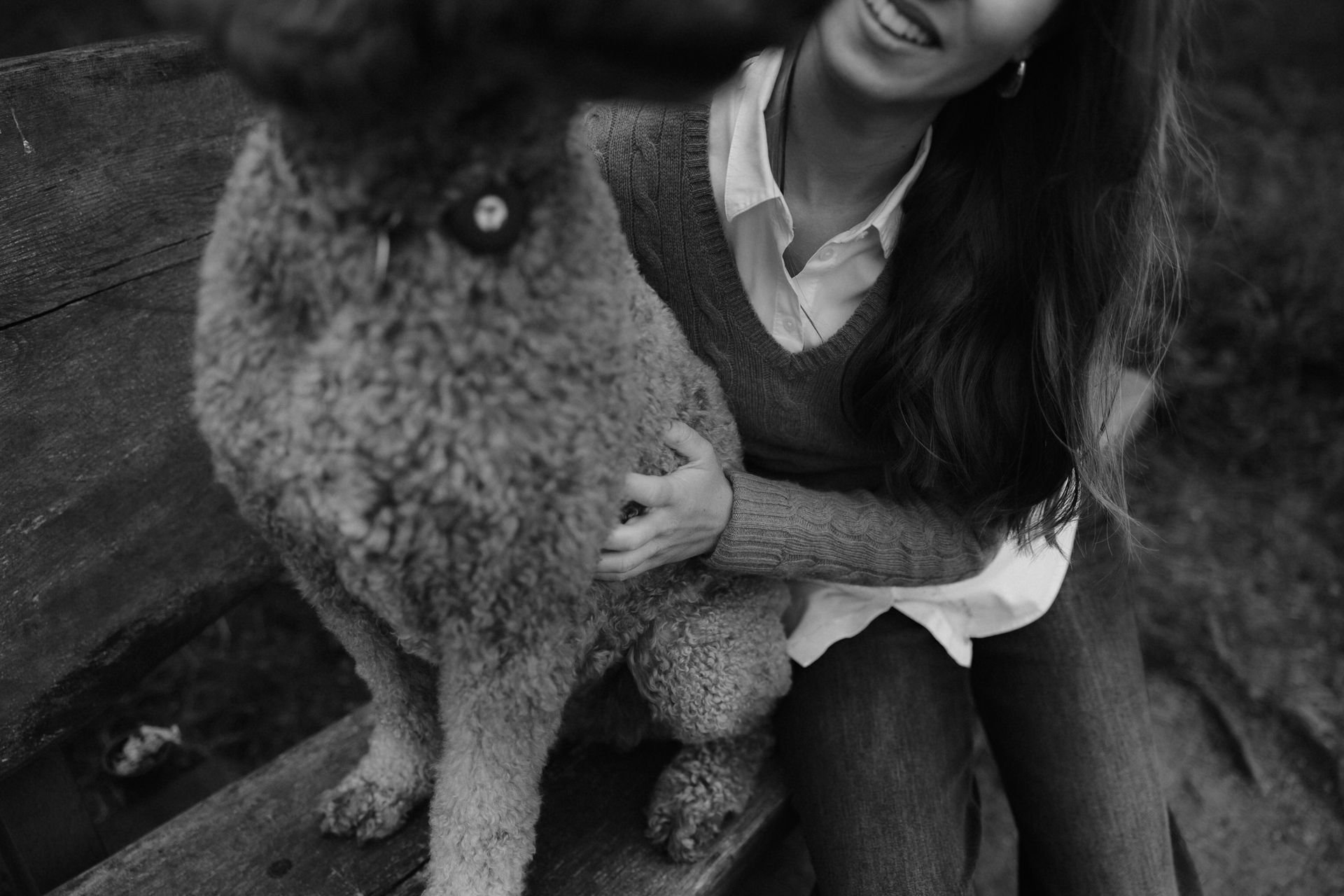 Schwarz-Weiß-Aufnahme einer lachenden Frau, die mit ihrem Hund auf einer Holzbank sitzt und ihn liebevoll festhält