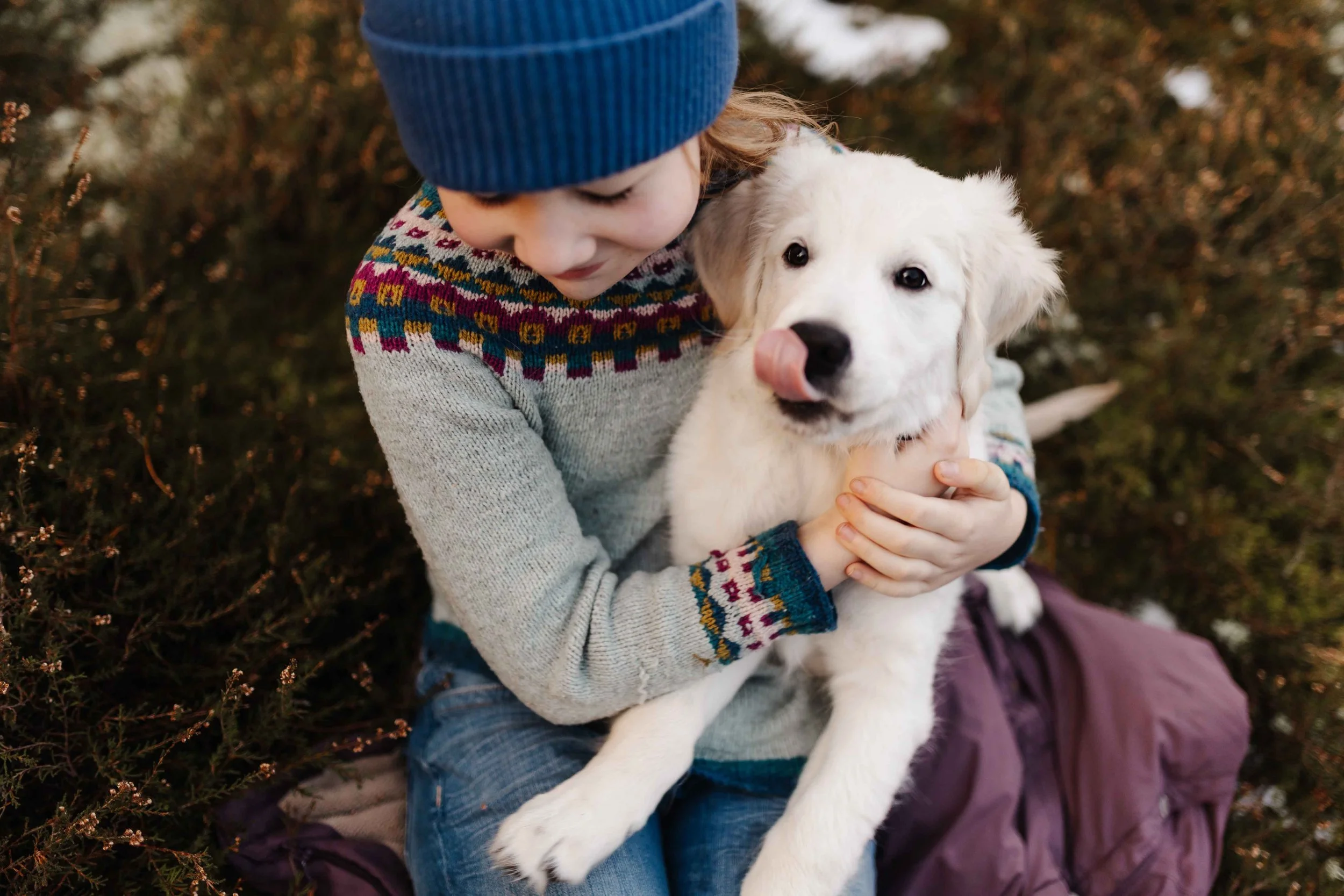 Mädchen kuschelt liebevoll mit Golden Retriever Welpen im Winter auf einer Wiese.