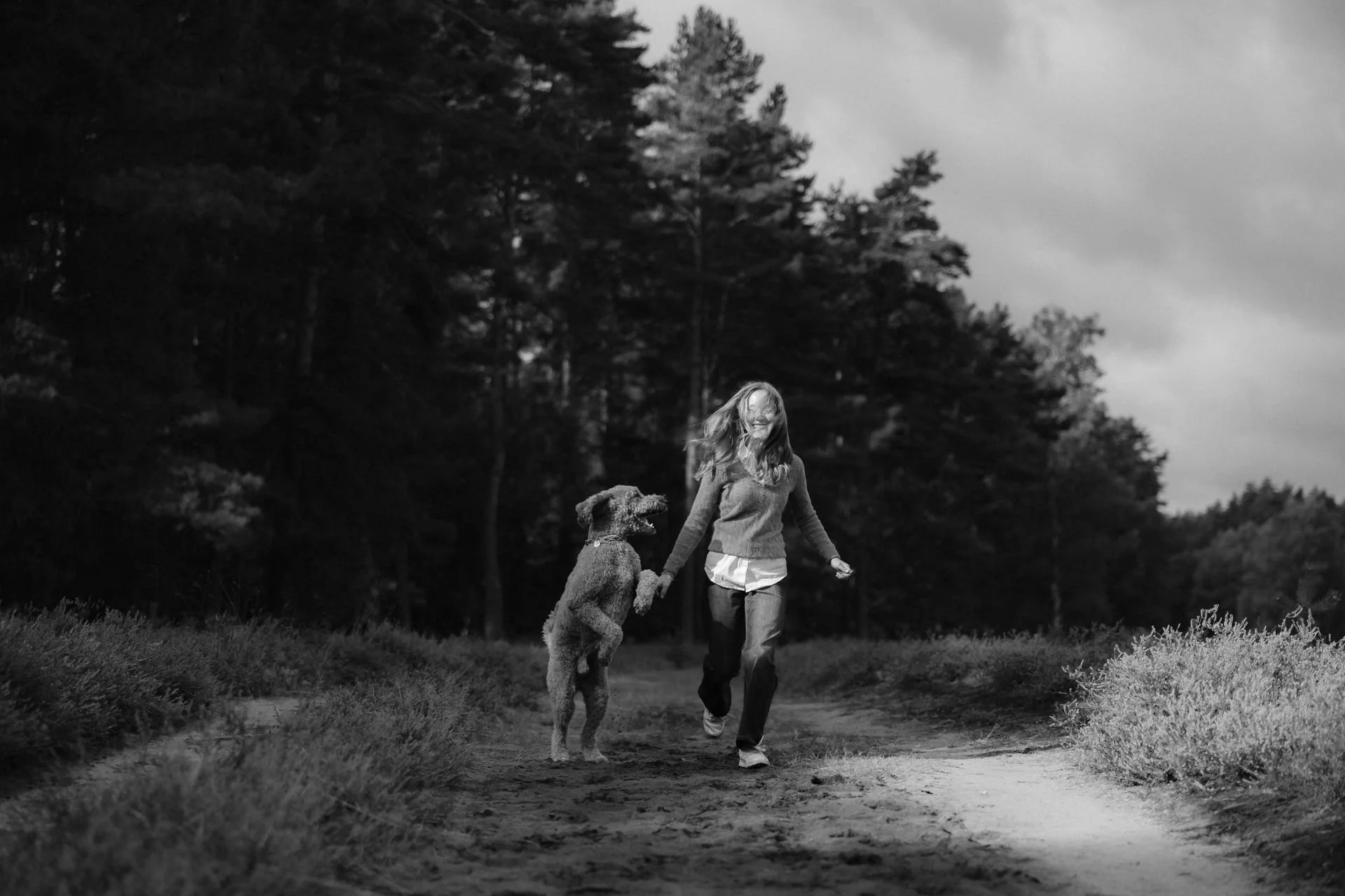 Frau läuft mit ihrem Hund durch die Heidelandschaft, während der Hund spielerisch an ihrer Hand hochspringt