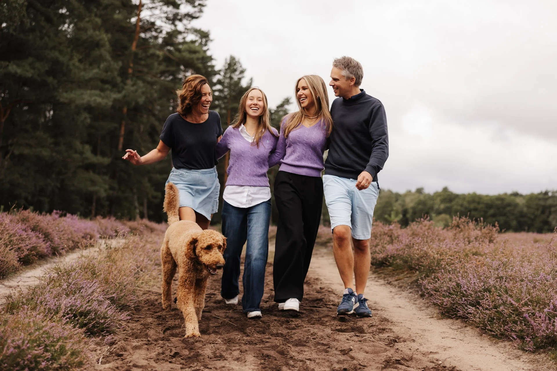 Familie spaziert gemeinsam mit ihrem Hund durch eine blühende Heidelandschaft