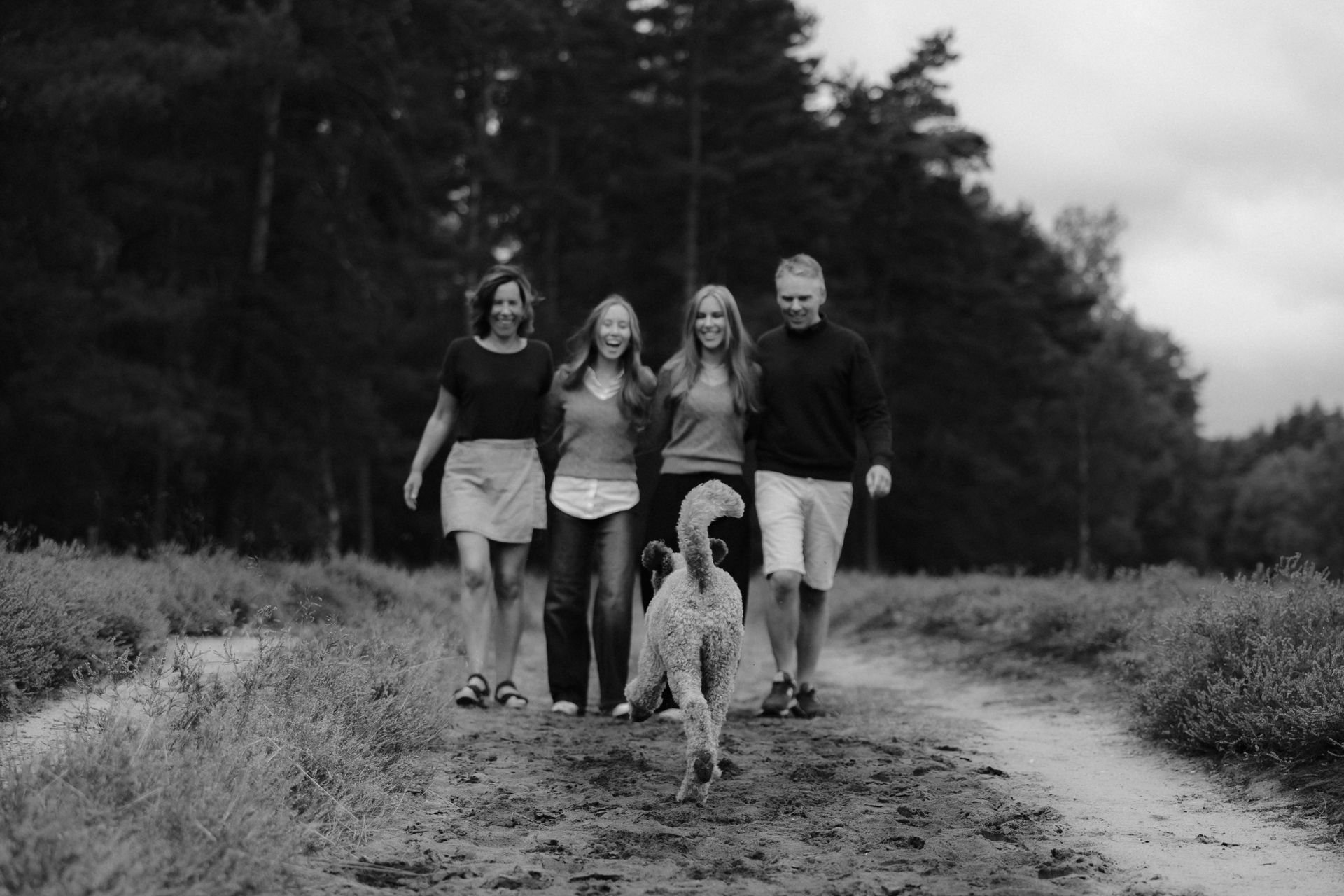 Familie spaziert mit ihrem Hund auf einem Weg durch die Heidelandschaft, fotografiert in Schwarz-Weiß