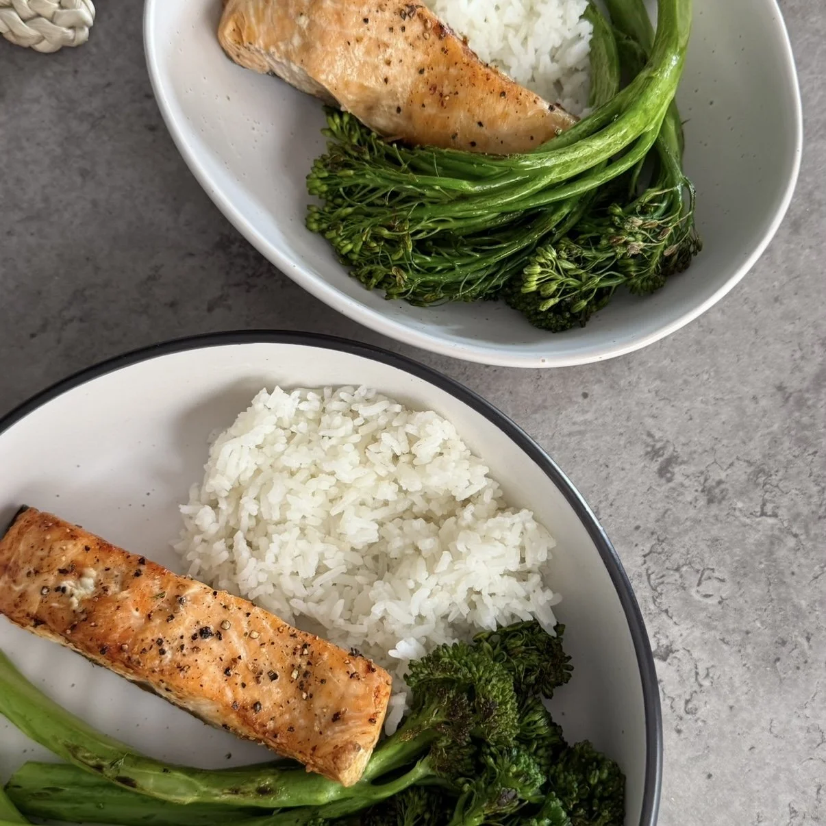 Platos con arroz, salmón a la parrilla, brócoli y espárragos en tazones blancos.