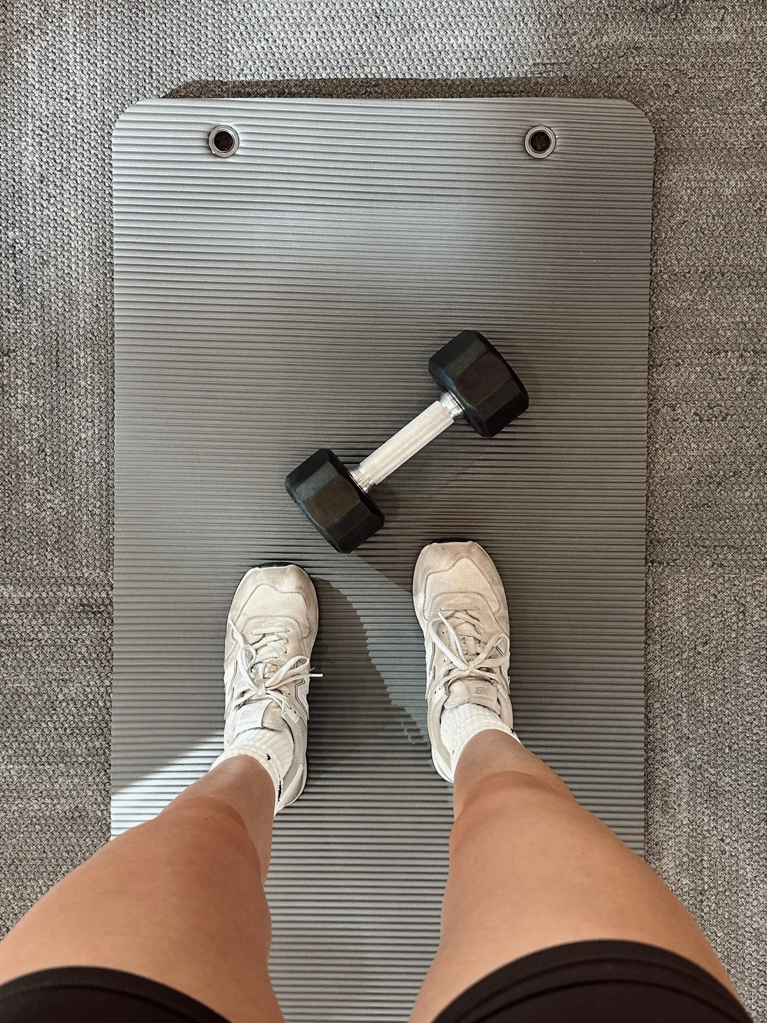 Persona de pie en una cinta de correr, con pesas y zapatos deportivos blancos.