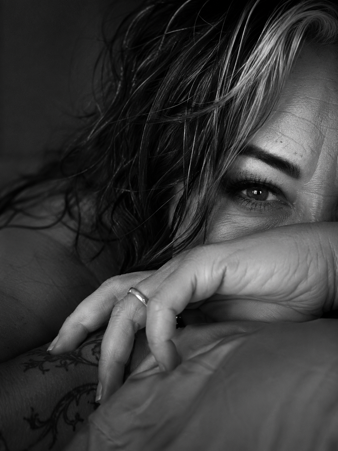 Close-up black and white photograph of a woman with wet hair partially covering her face, with one eye visible and her hand resting near her lips.