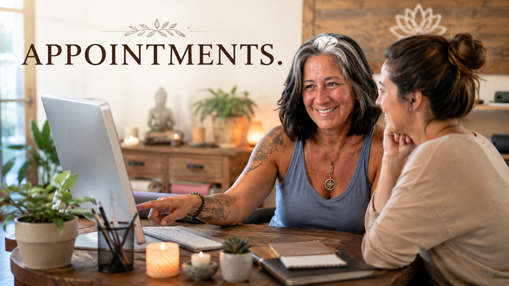 Two women sitting at a wooden table having a conversation, one pointing at a computer screen, with the word 'APPOINTMENTS.' written on the wall behind them, surrounded by plants, candles, and decorative items.