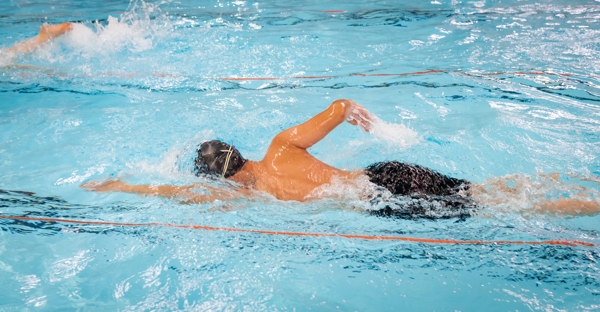 Swimmer doing the backstroke in a swimming pool with a black cap and goggles.
