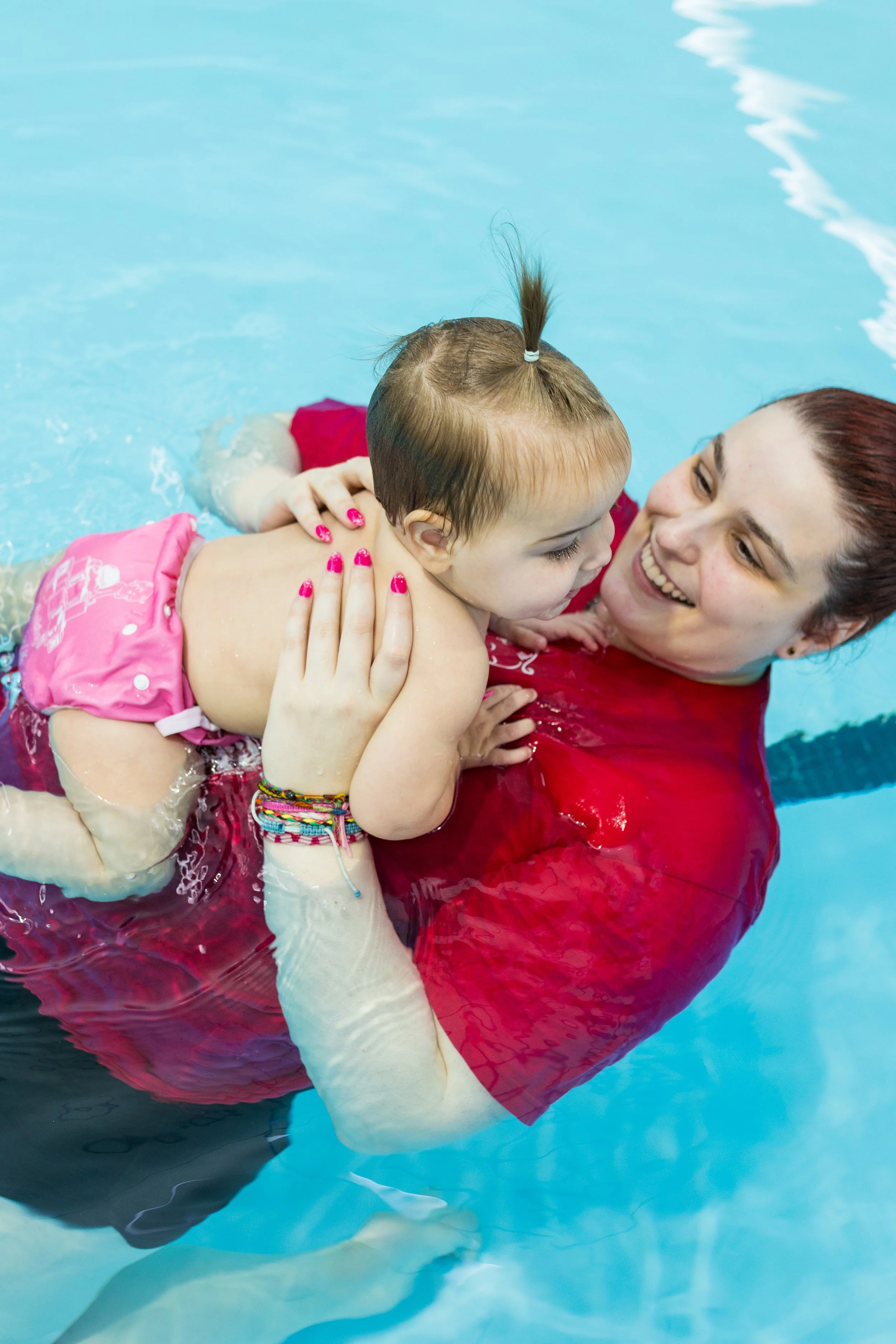 A woman and a young girl sharing a joyful moment in a swimming pool, with the woman holding the girl close as they smile at each other.