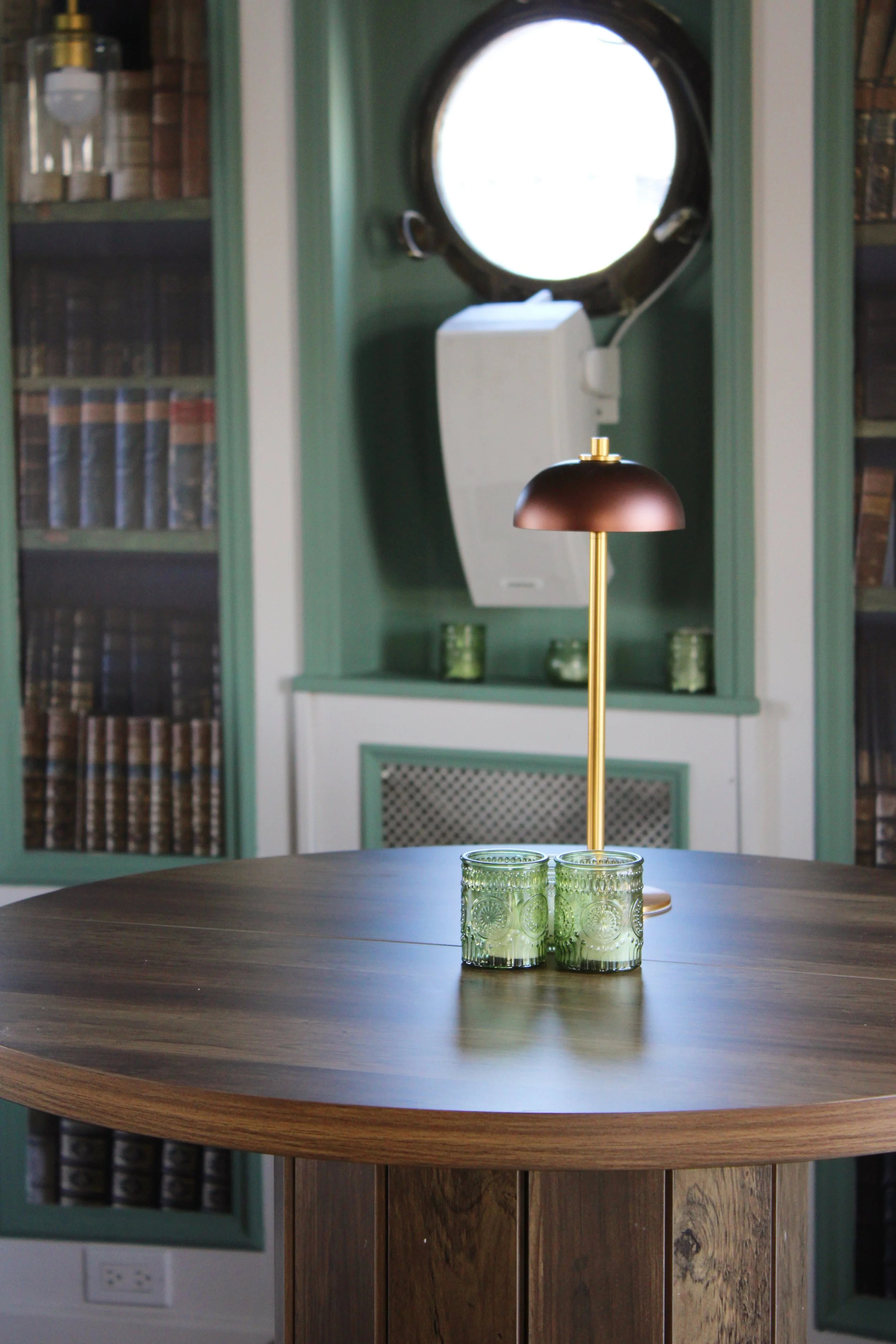 Interior of a historical library or museum room with wooden tables, brass lamps, and built-in bookshelves filled with books. A display stand with information about the Northwind ship is in the foreground. Large arched glass door and windows are in the background.