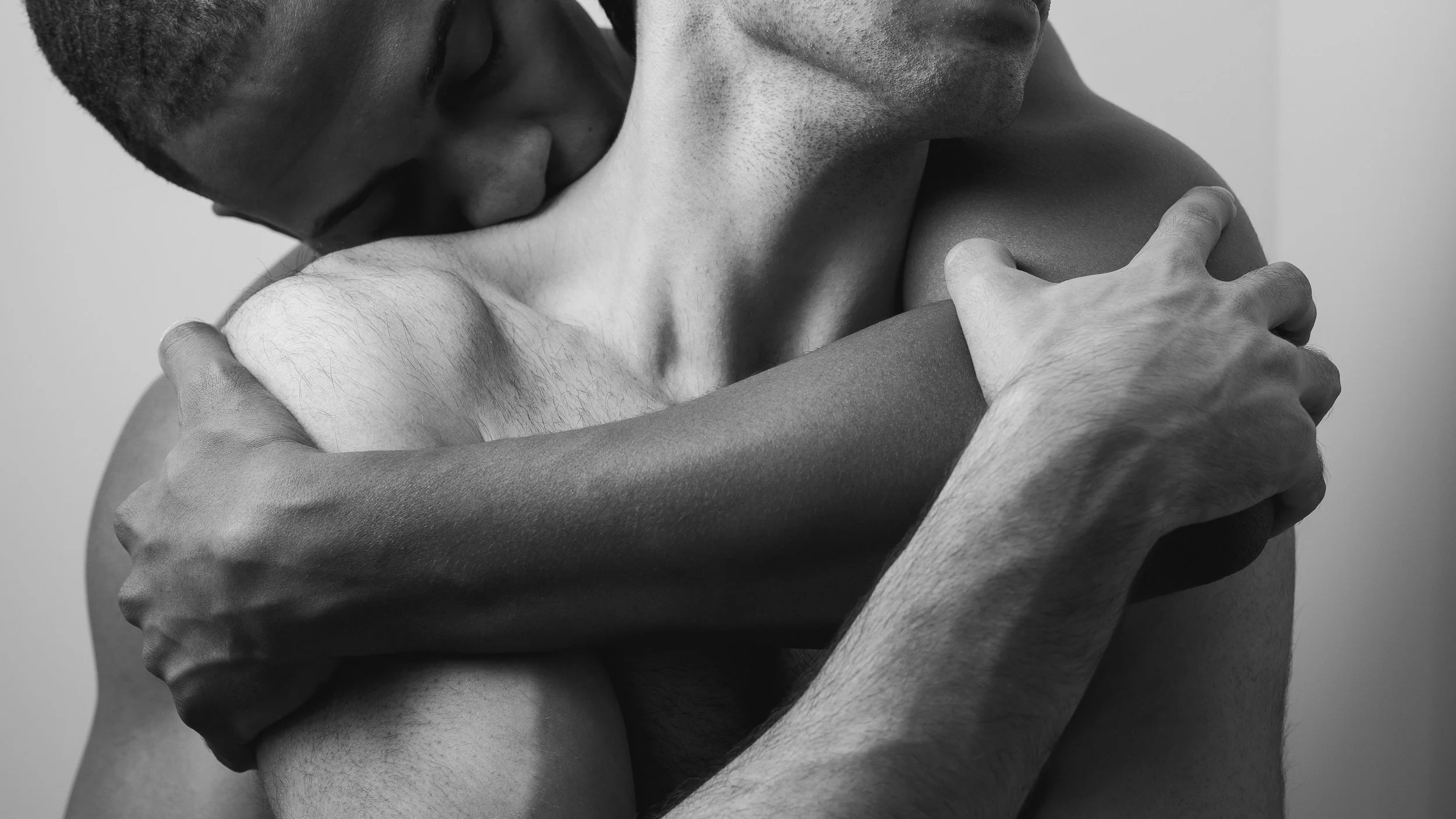 A black and white photo of two men embracing. One man is resting his head on the other's shoulder, and they are holding each other tightly.