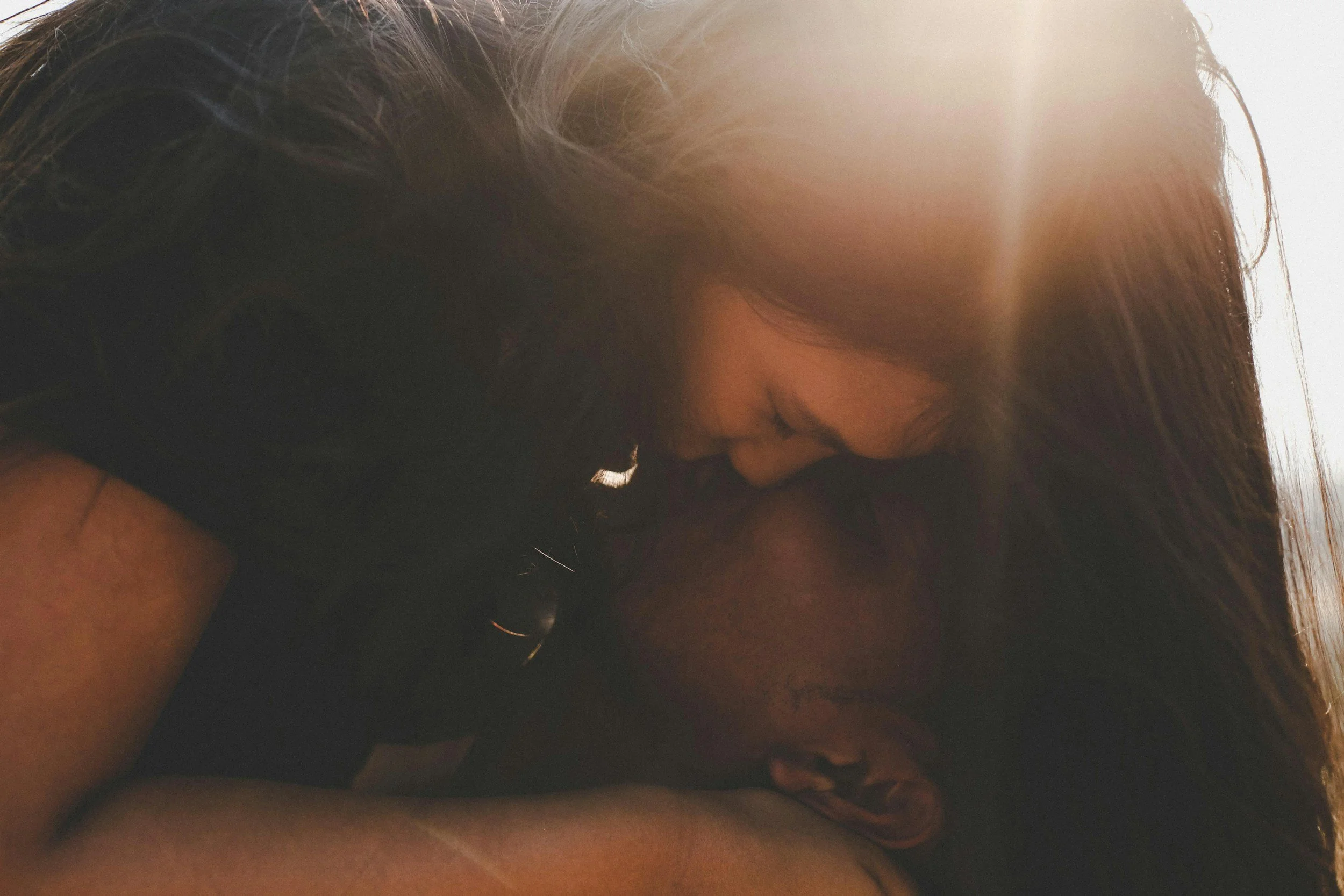 Two women hugging and resting their foreheads together in front of sunlight.