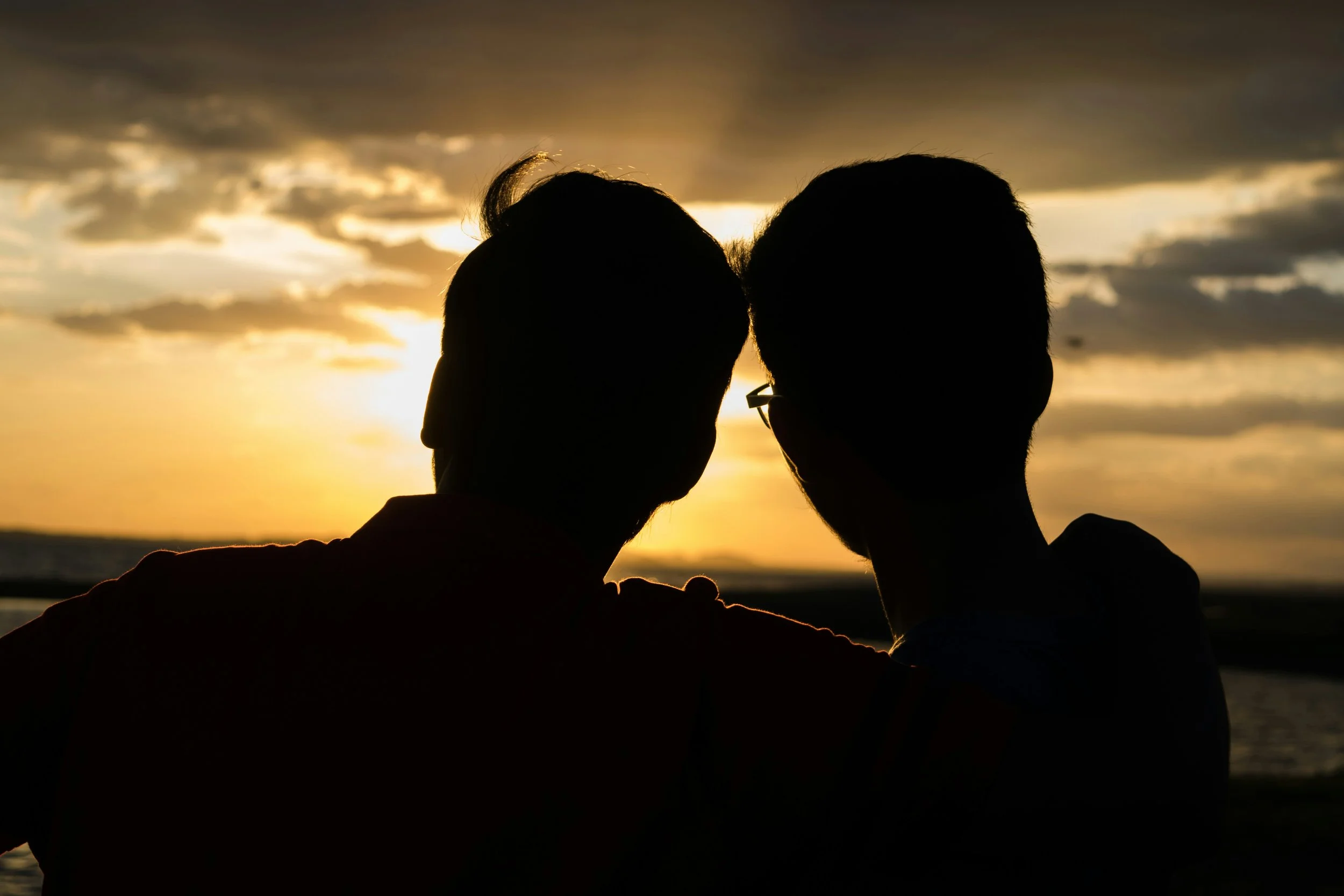 Couple sitting in a golden field at sunset with an arm around each other, representing ketamine assisted couples therapy
