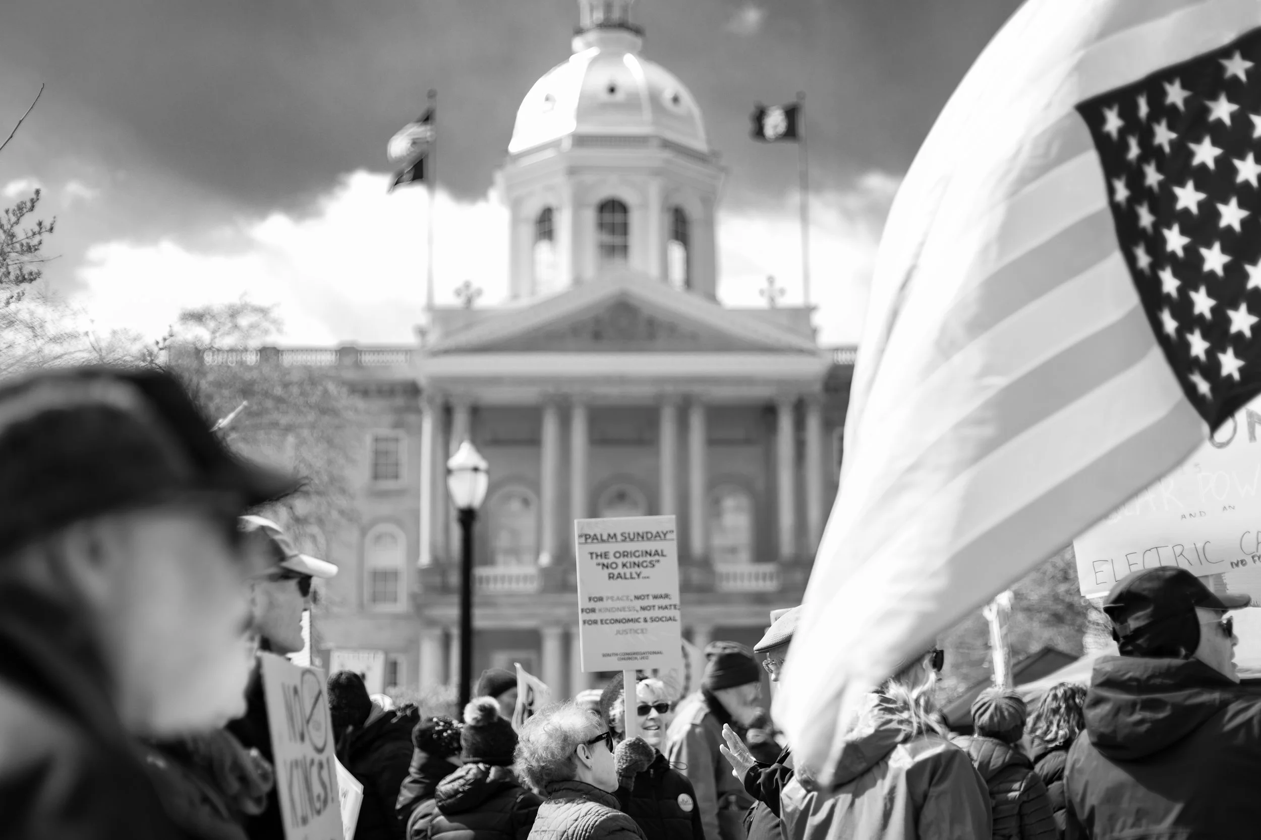 A crowd of people protesting during a rally, holding signs and flags, with a large government building in the background.