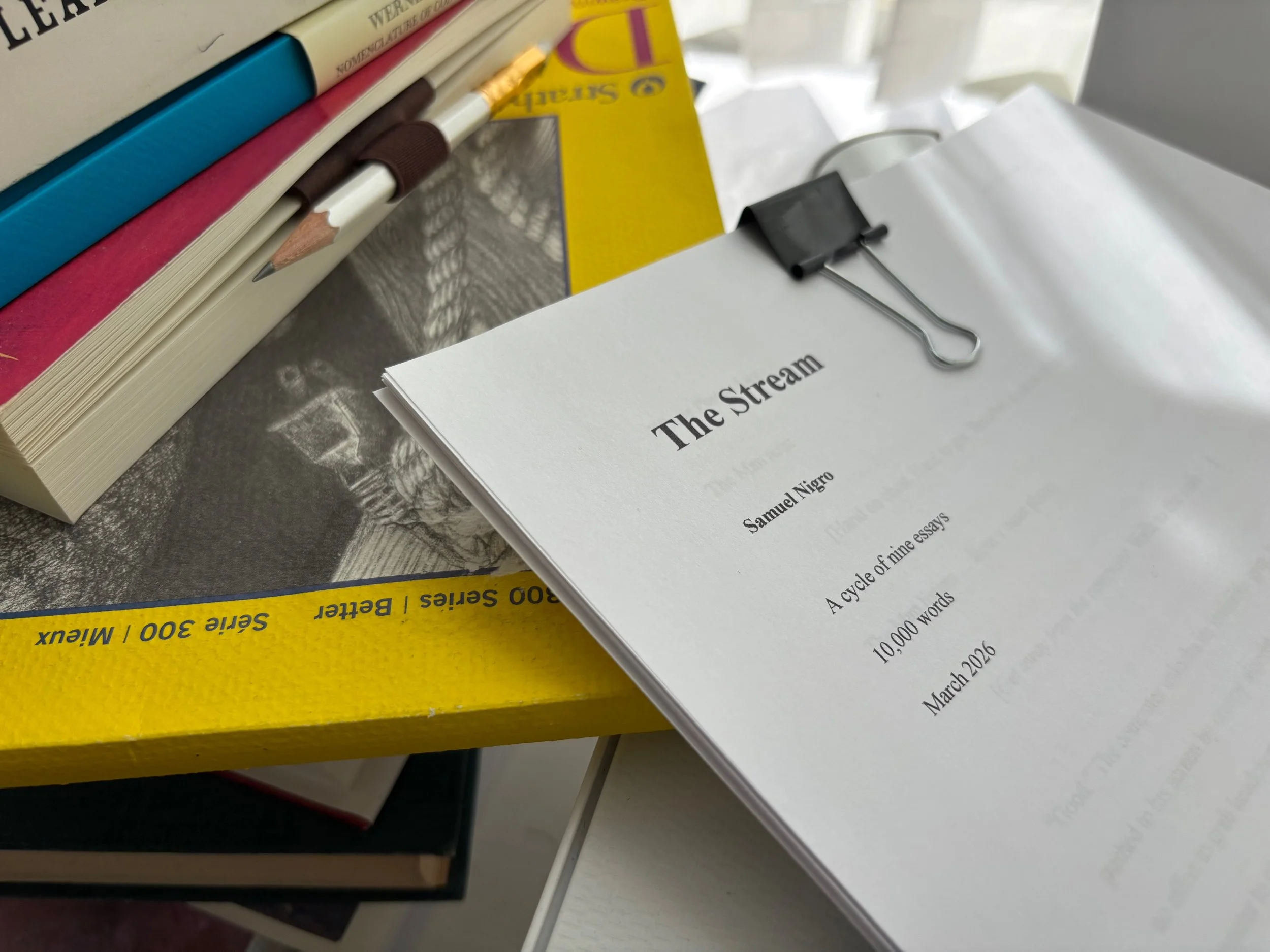Printed manuscript of The Stream by Samuel Nigro resting on a stack of books and notebooks.