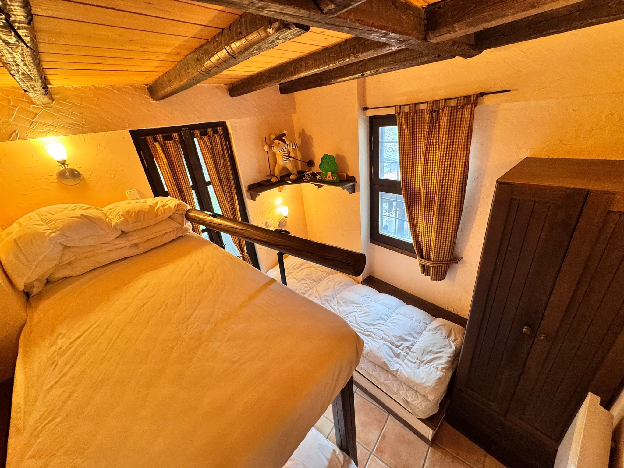 A cozy attic bedroom with a bed, small window, shelves with stuffed toys, and wooden beams on the ceiling.