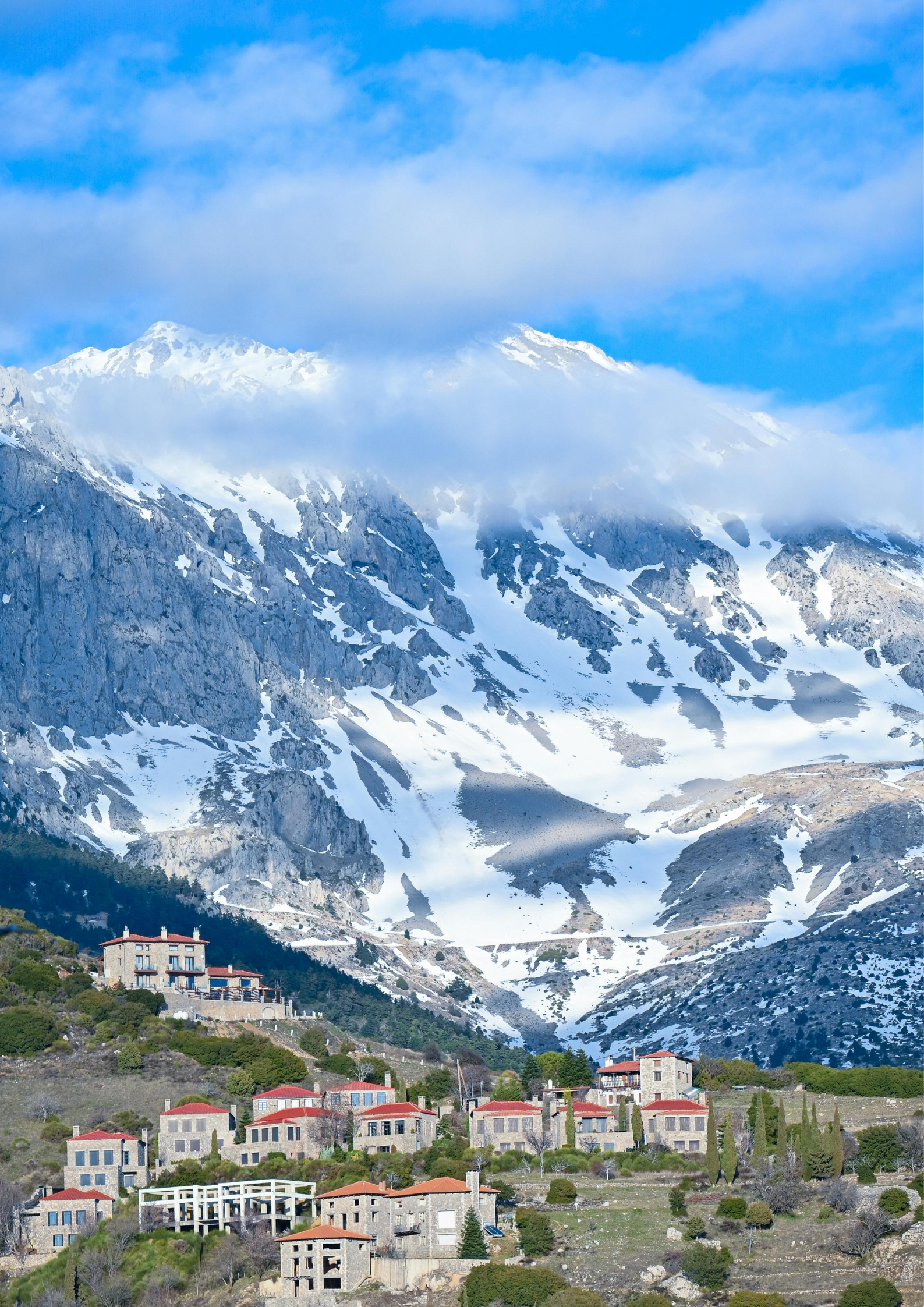 Mountain landscape with snow-covered peaks and a small village at the base, under a partly cloudy sky.