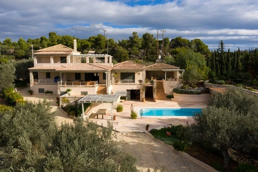 Large house with multiple levels, tiled roof, and spacious balconies, surrounded by trees, with a swimming pool and outdoor seating area in the backyard.