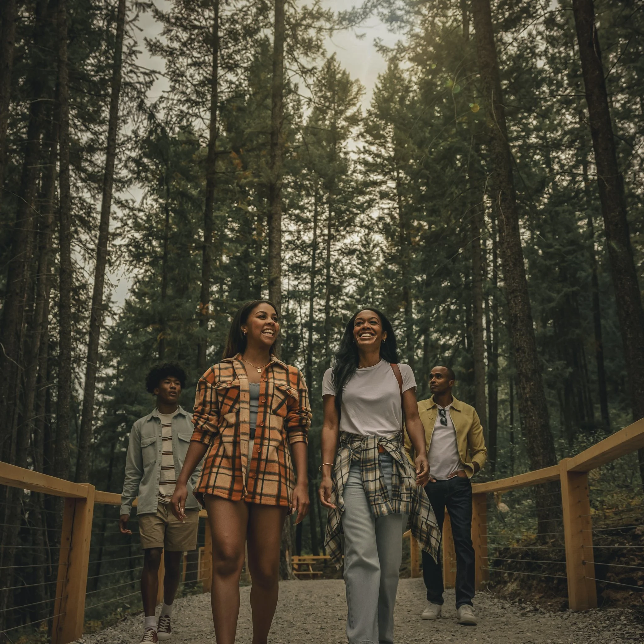 Four people walking and smiling along a forest trail with tall trees in the background.
