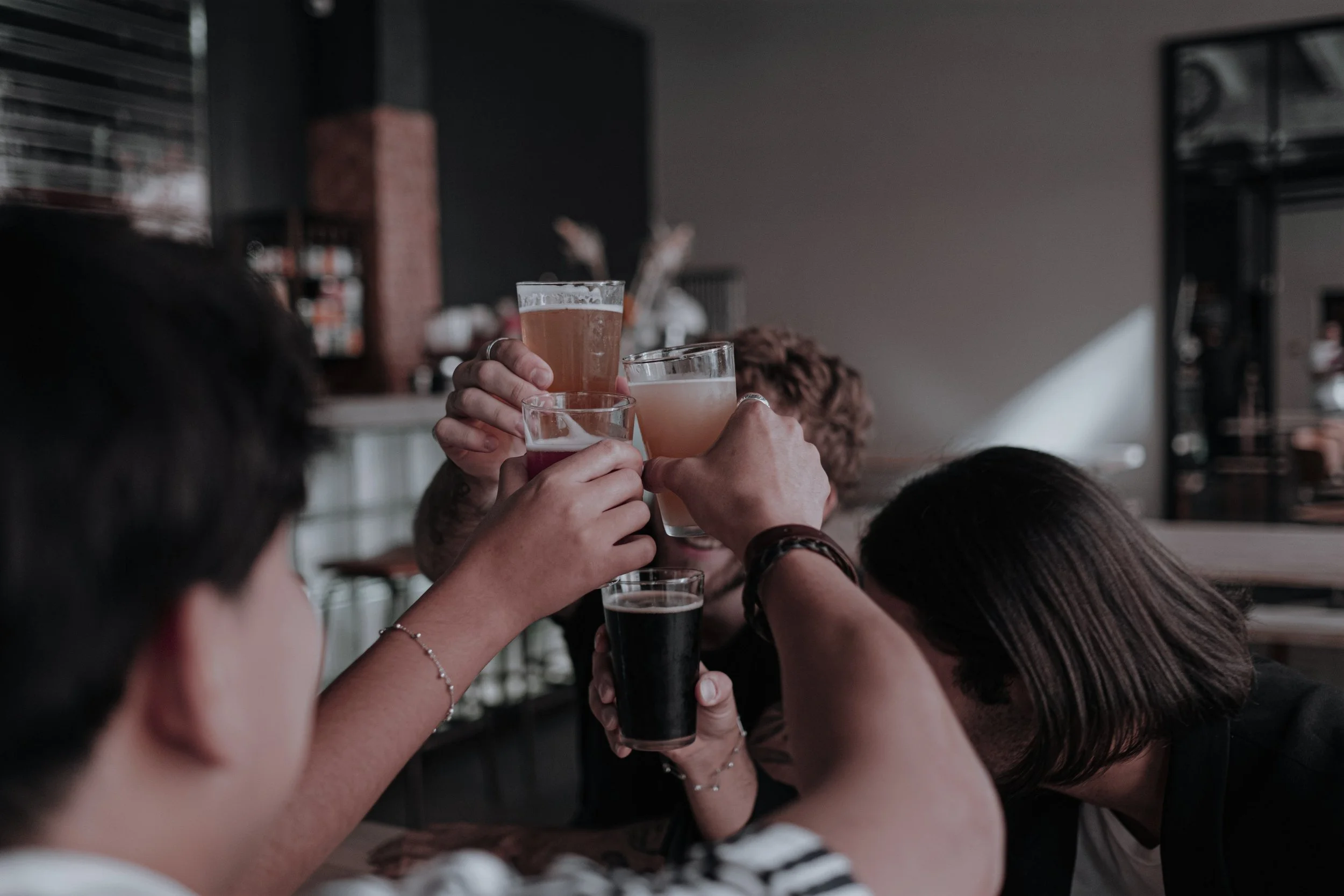 Group of friends raising and toasting glasses of various beverages in a bar or pub setting.