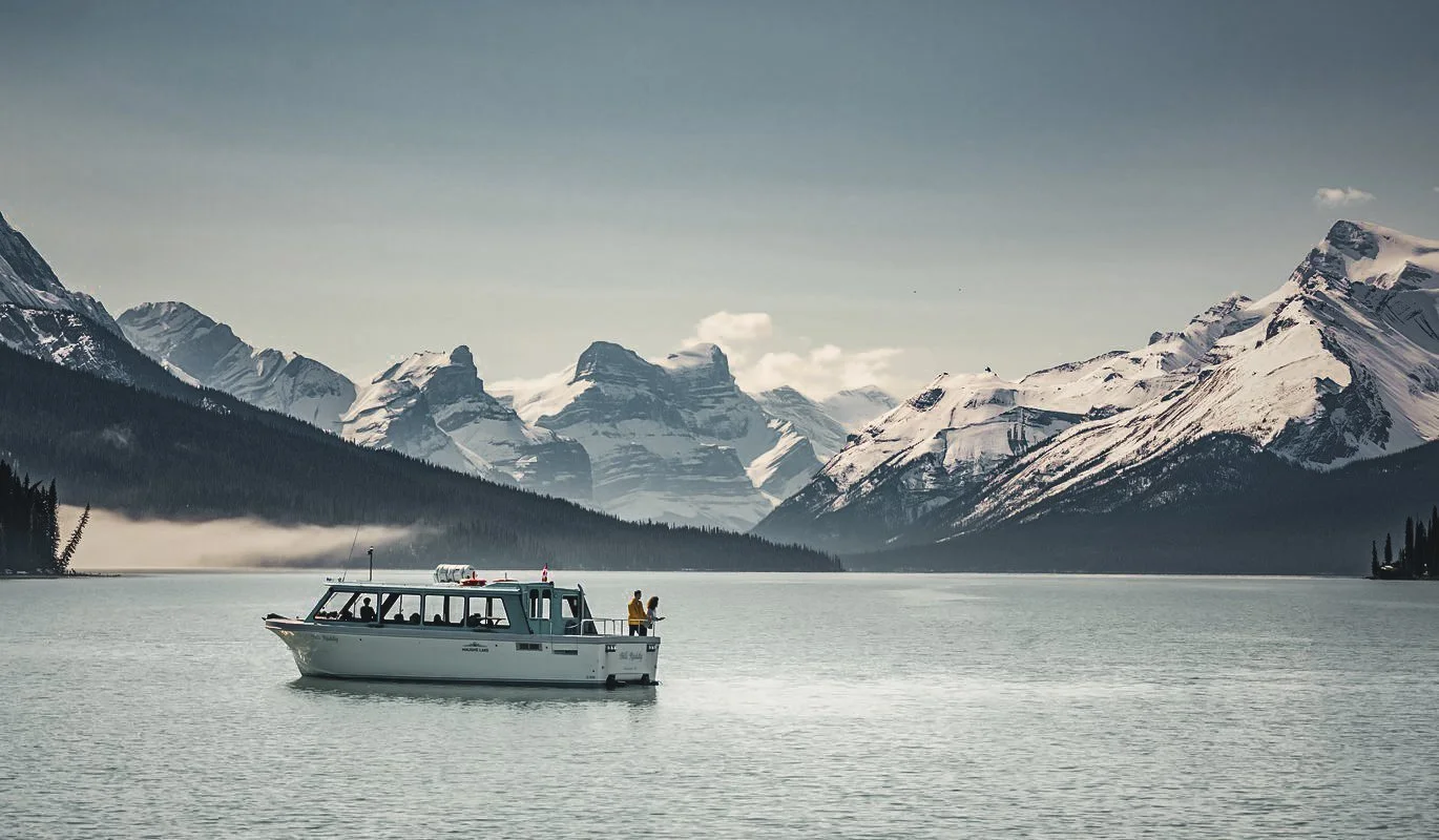 A boat on a calm lake with snow-capped mountains in the background.