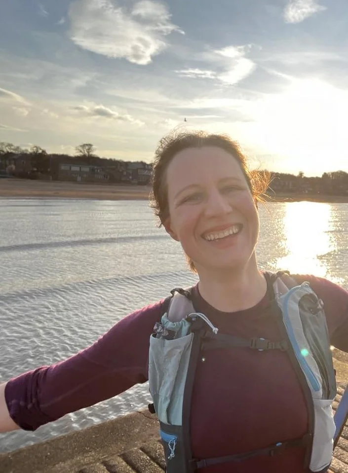 Mia, smiling with arms outstretched near Portobello beach. Taking a moment to enjoy the sunset during her run.