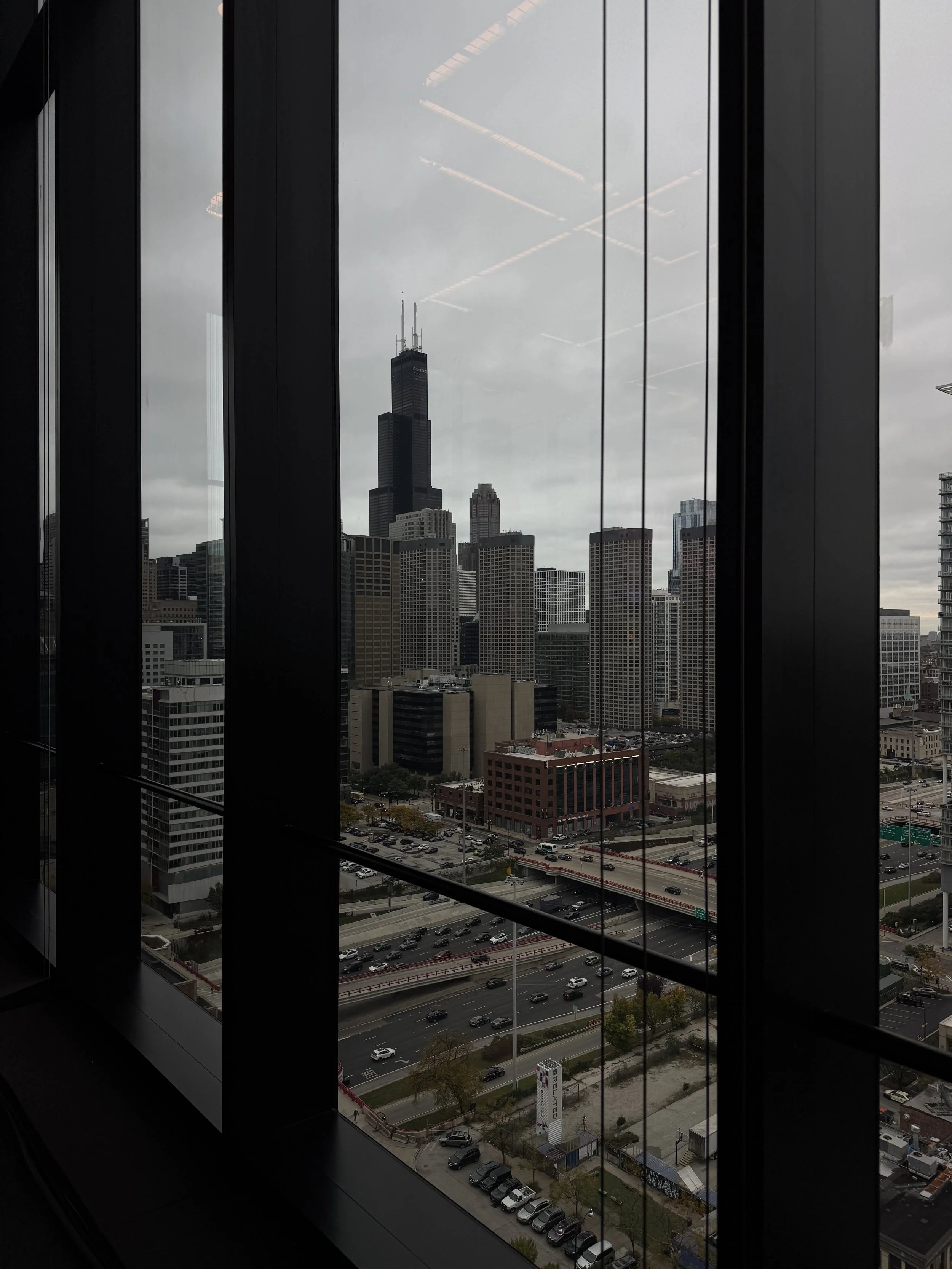A view of a cityscape of Chicago, with the Willis Tower visible through window panels, overcast sky, busy roads, and tall buildings.