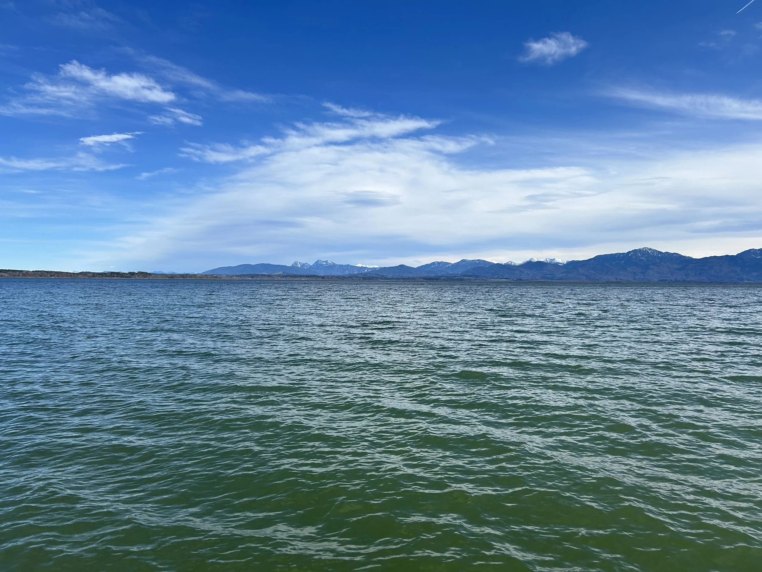 Blick auf einen See mit Bergen im Hintergrund und einem blauen Himmel mit Wolken.