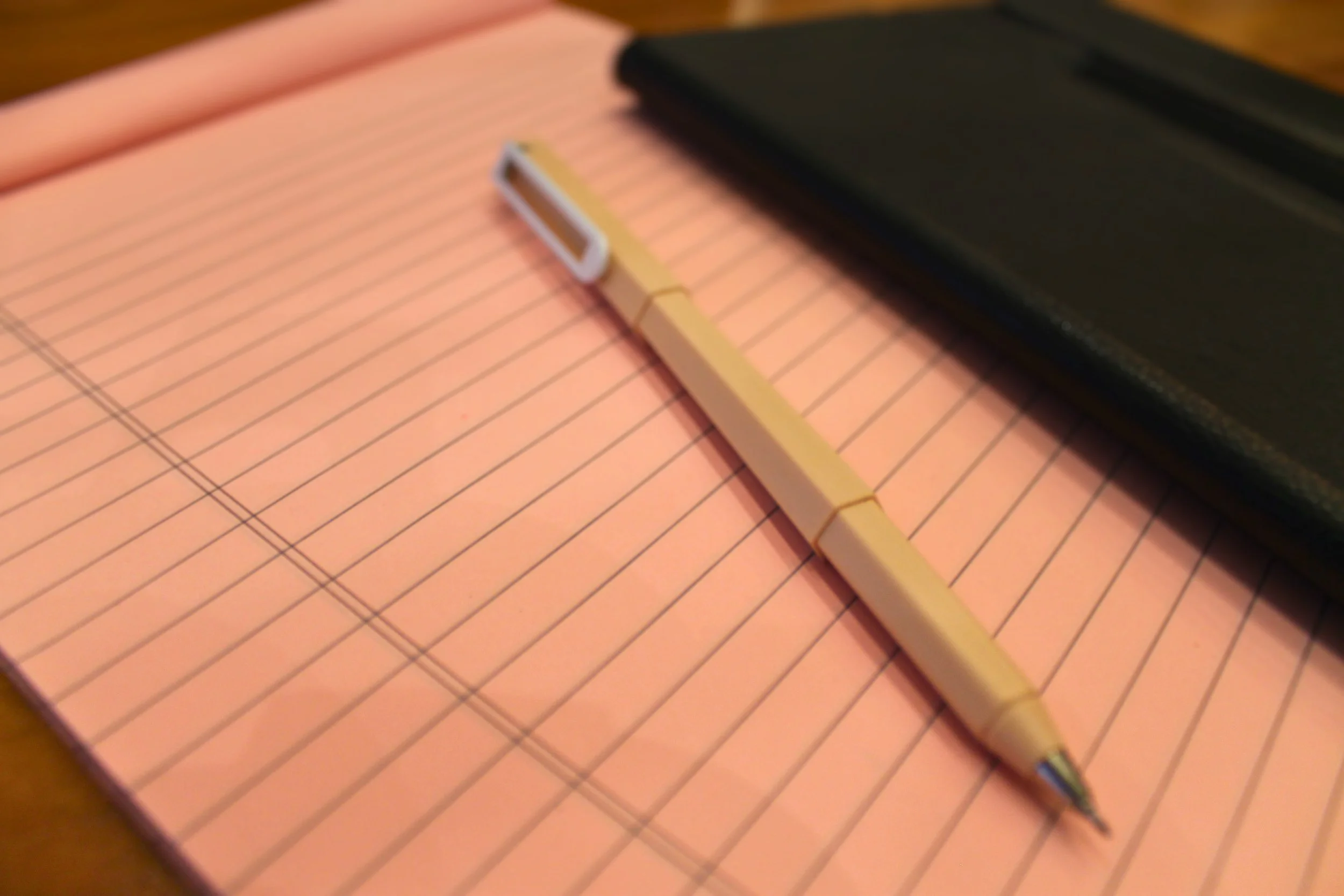 Pink lined notebook with a tan pen and an ipad on a wooden surface, for taking notes during discovery calls or consultations.