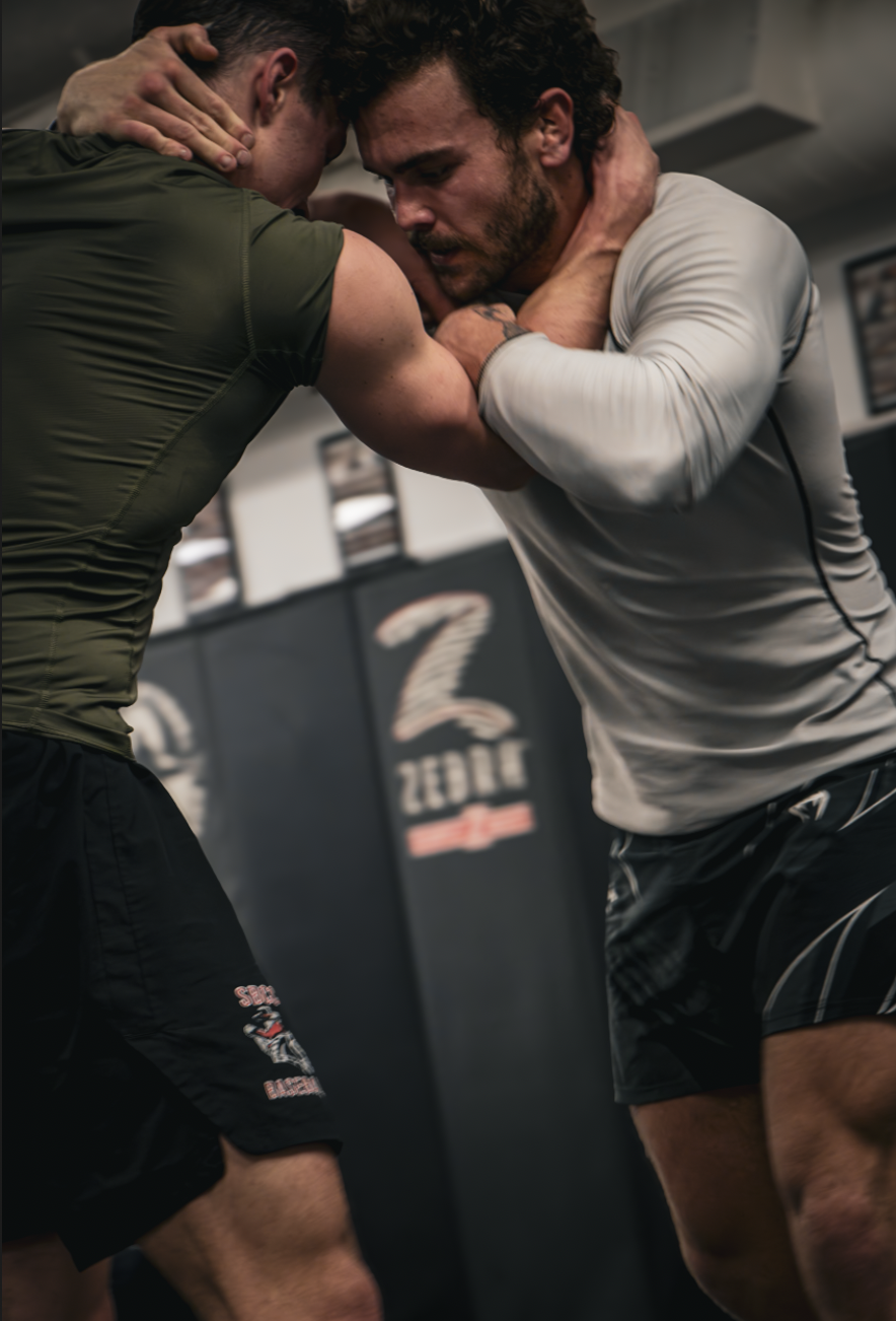 Two men practicing Brazilian Jiu-Jitsu on the mat, engaged in a grappling hold at the gym.
