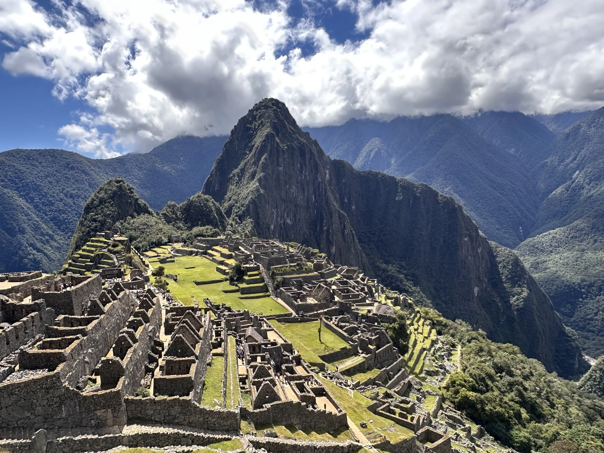 Ancient Incan ruins of Machu Picchu with stone structures and terraces in the mountains under a partly cloudy sky.