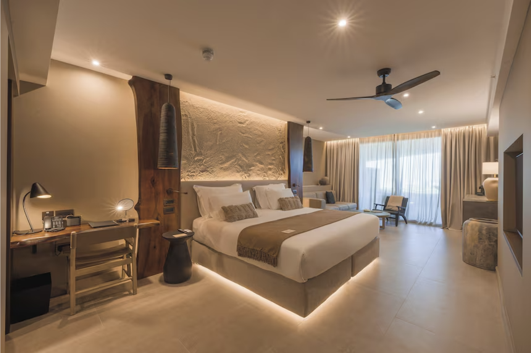 Luxury hotel bedroom with a large bed, bedside tables, desk, seating area, and large window with curtains.