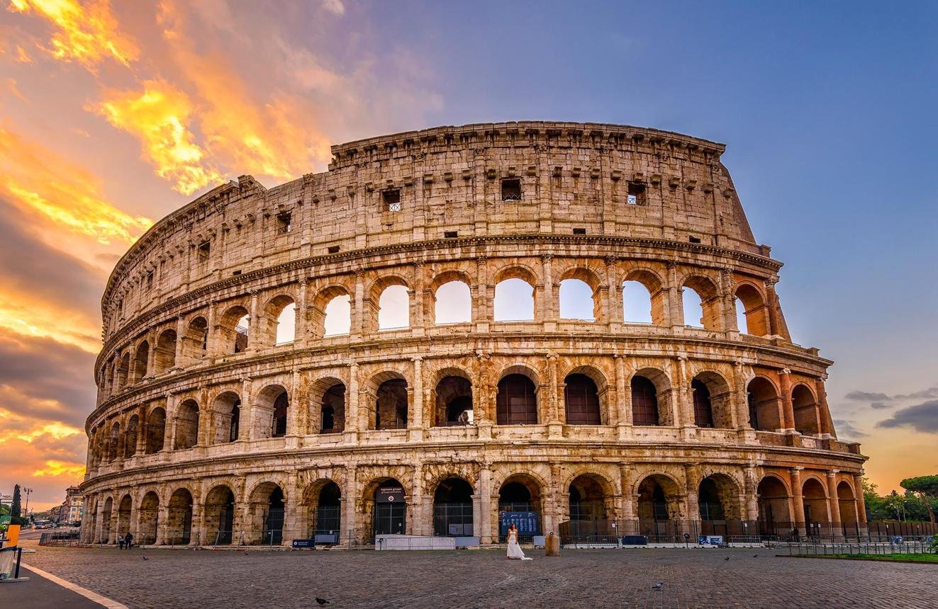 The Colosseum, an ancient Roman amphitheater, at sunset with vibrant orange and pink sky