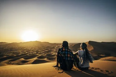 Moroccan desert at sunrise with glowing dunes, soft light, and one or two people silhouetted in the landscape.