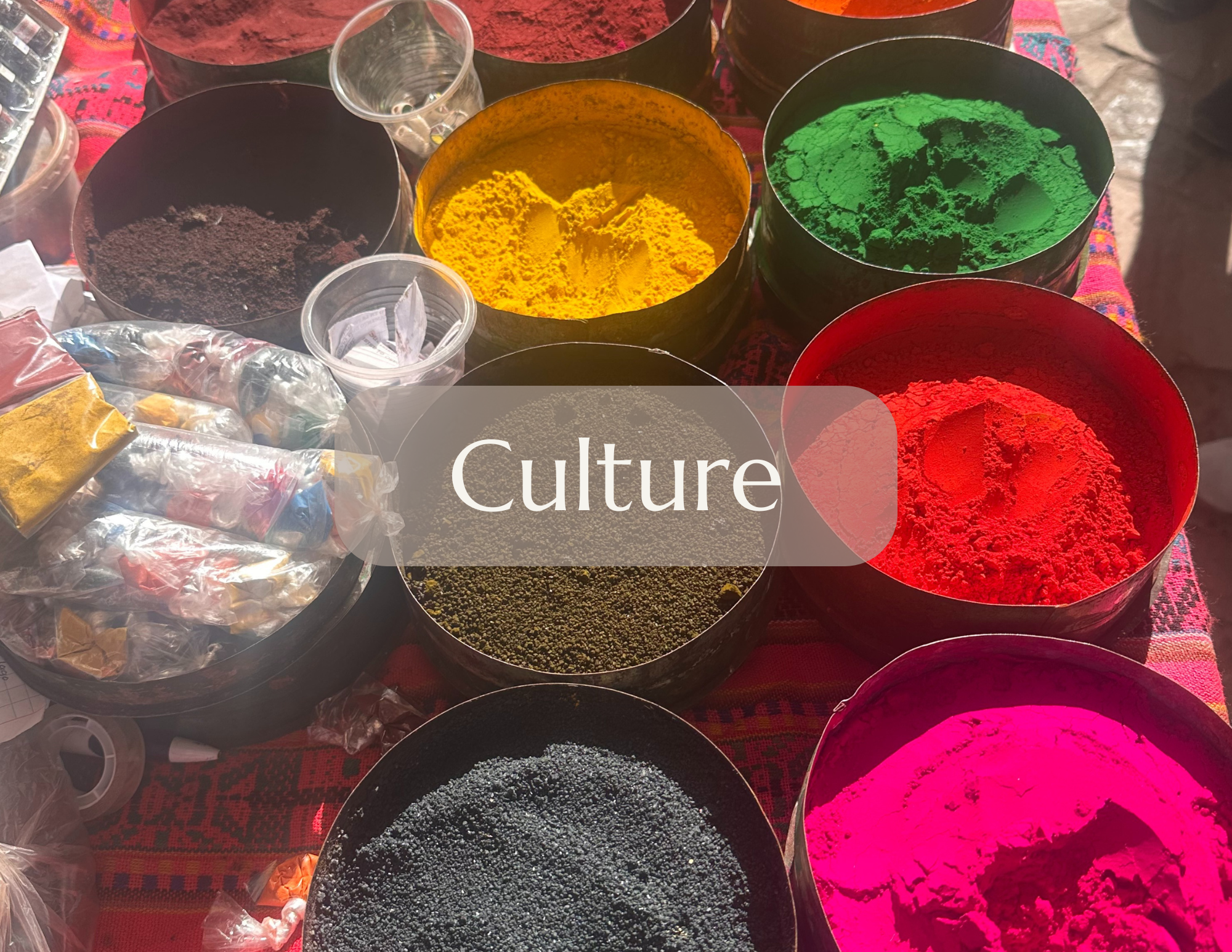 Colorful powders of red, green, yellow, black, pink, and orange in open containers on a table, with small plastic bags and measuring spoons. These powders are used in traditional cultural celebrations.
