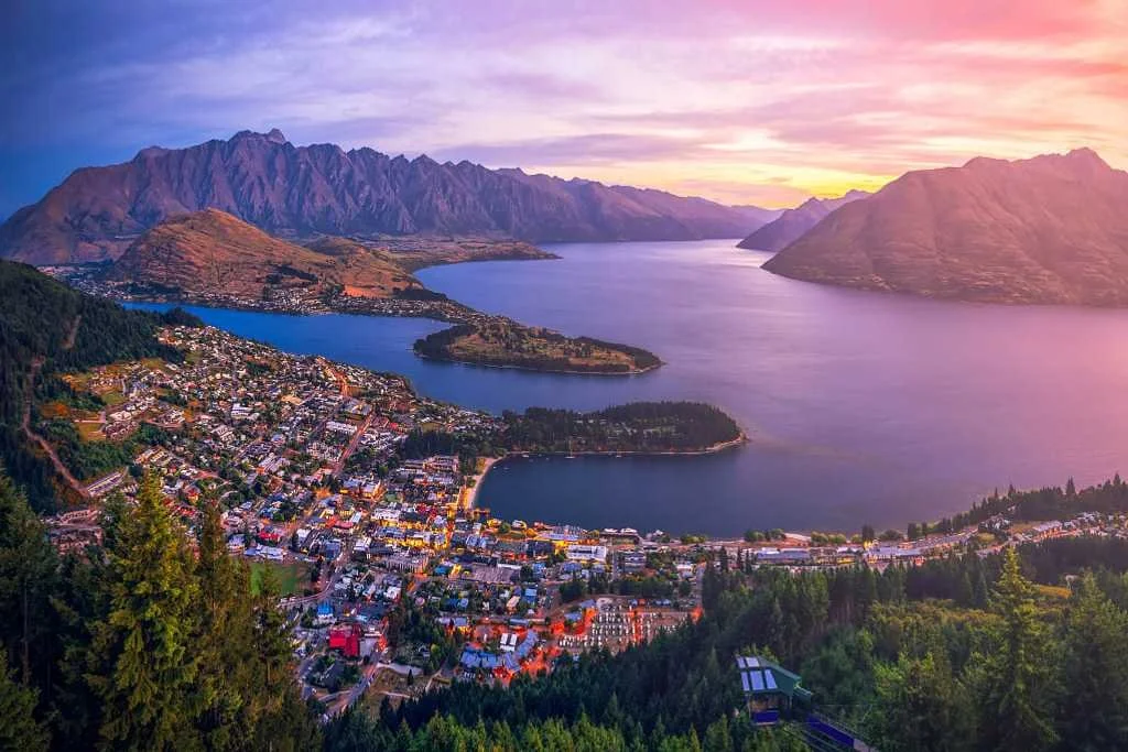 Aerial view of a town beside a large lake surrounded by mountains at sunset with a colorful sky.