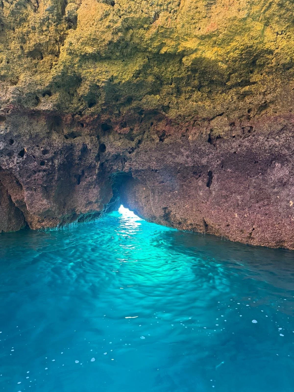 Sea cave with clear turquoise waters and light shining through the opening in the rock formation.