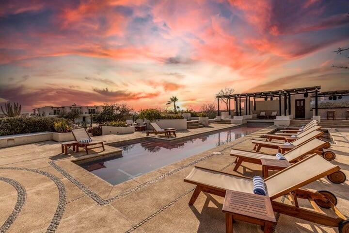 A rooftop pool area at sunset with several lounge chairs and a pergola.