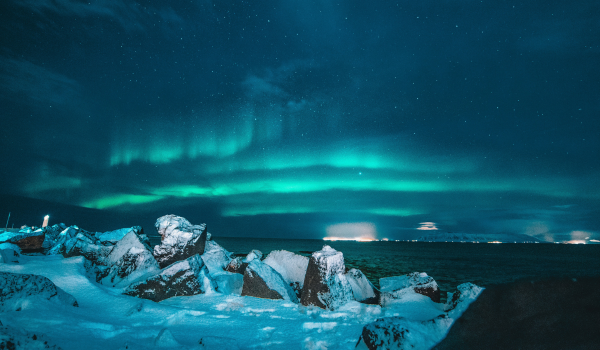 Snow-covered rocks on a shoreline with the northern lights in the night sky