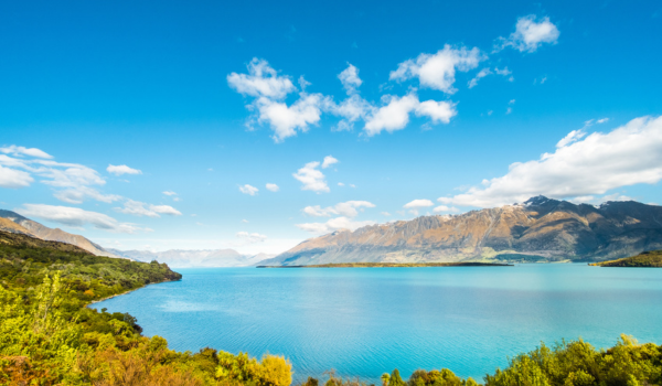 A large lake surrounded by green vegetation and mountains under a partly cloudy sky.
