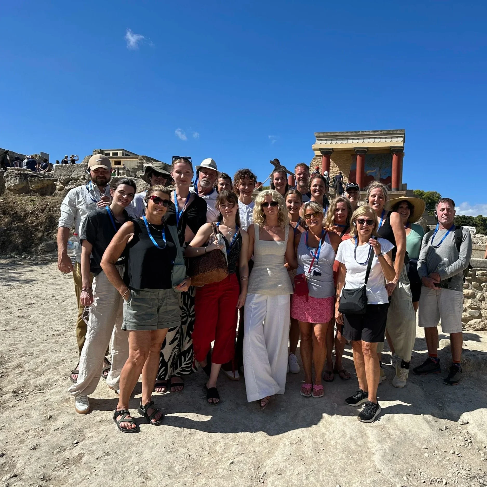 Group of tourists posing for a photo at an outdoor historical site under a blue sky, with ruins and columns in the background.
