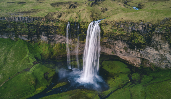 A tall waterfall cascading into a river surrounded by lush green landscape.