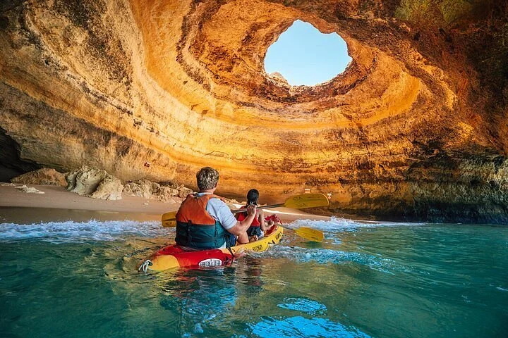 People kayaking inside a large sea cave with a circular opening at the top, revealing the sky.